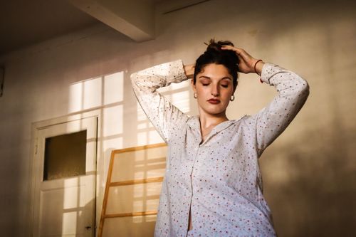 Free A woman stands with eyes closed in a sunlit room, exuding calm and peace. Stock Photo