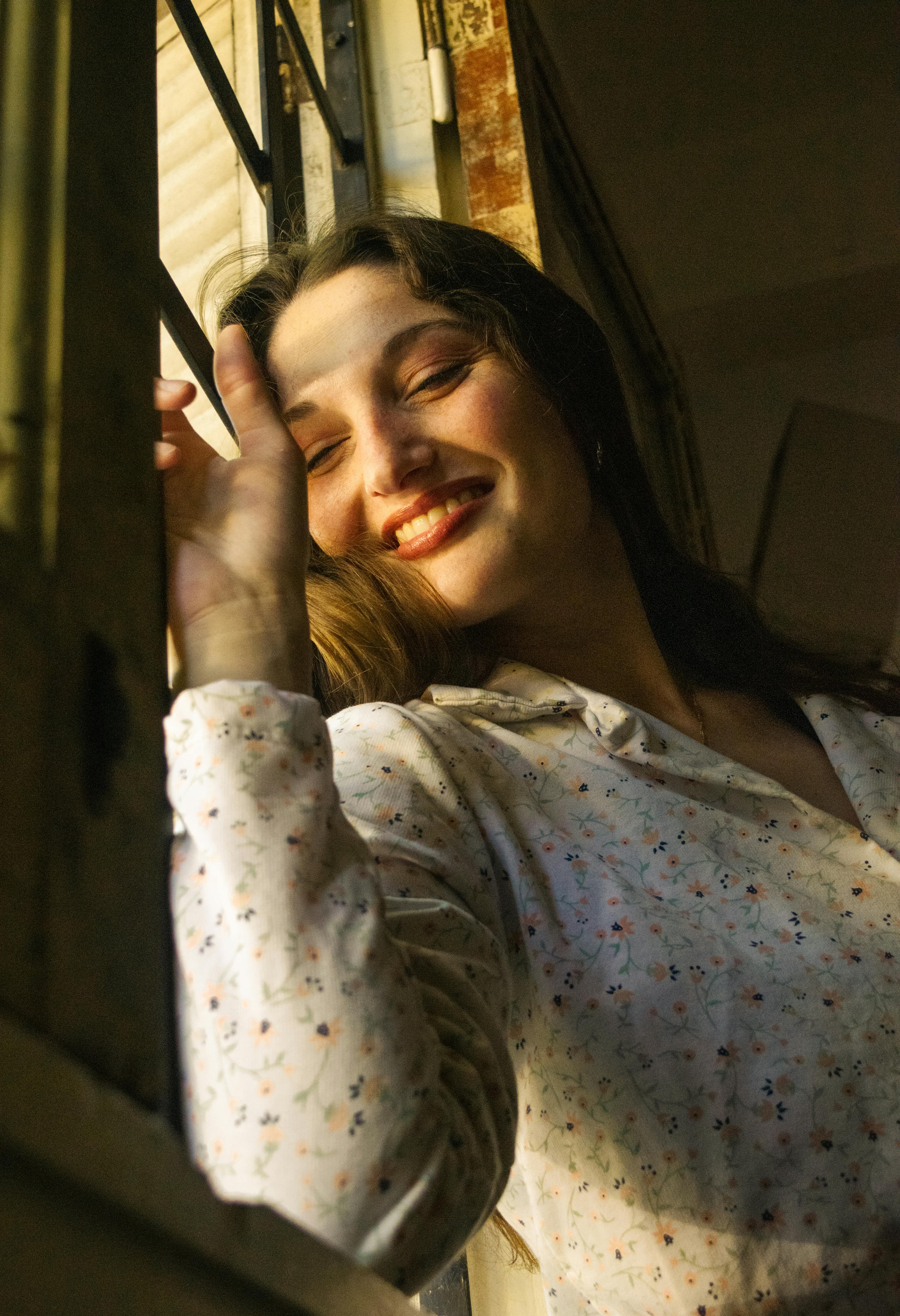 Gratuit Une jeune femme sourit chaleureusement en profitant de la lumière du soleil à l'intérieur. Photos