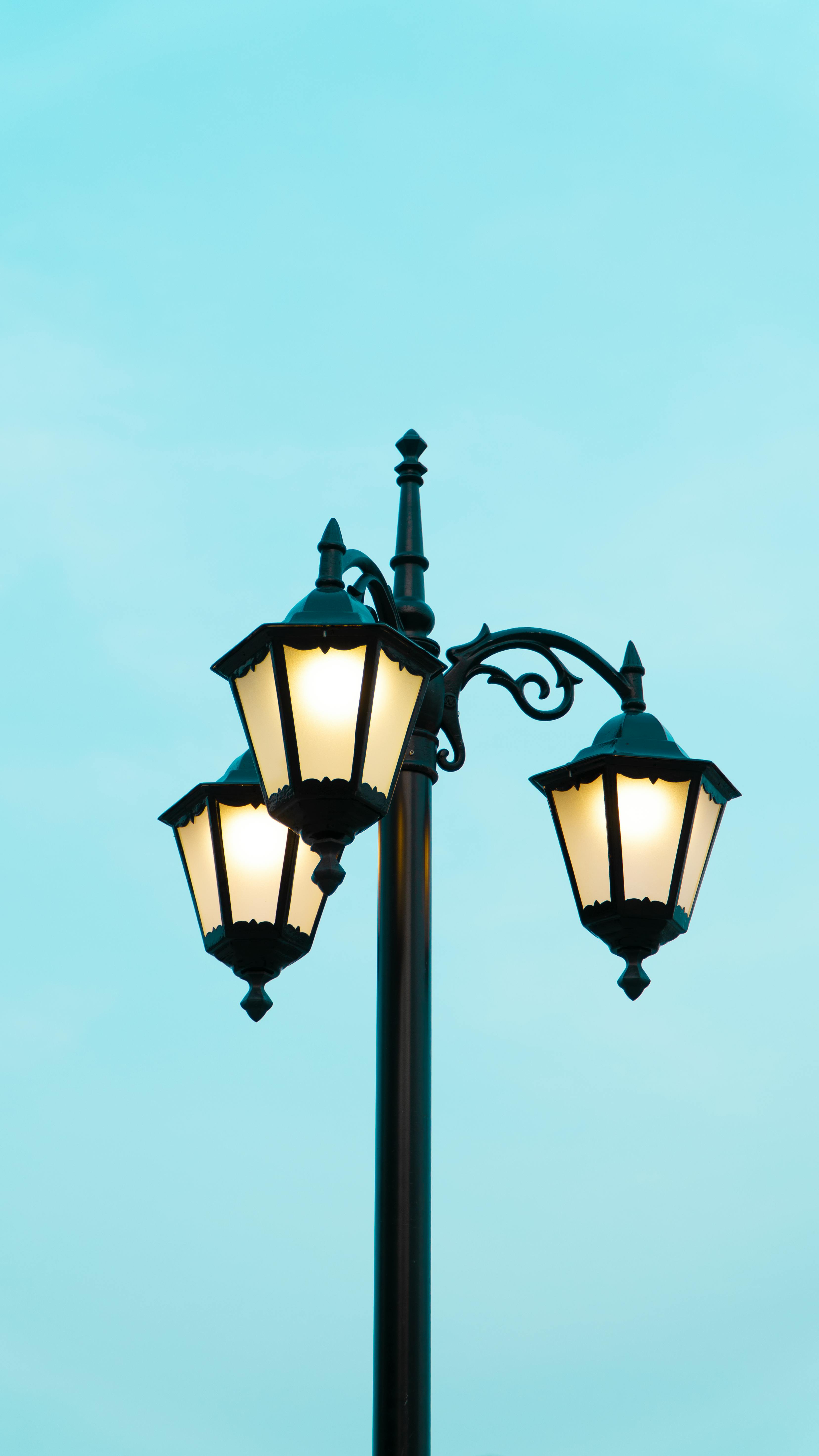 Free Classic vintage street lamp shining against a clear blue sky. Stylish urban decor. Stock Photo