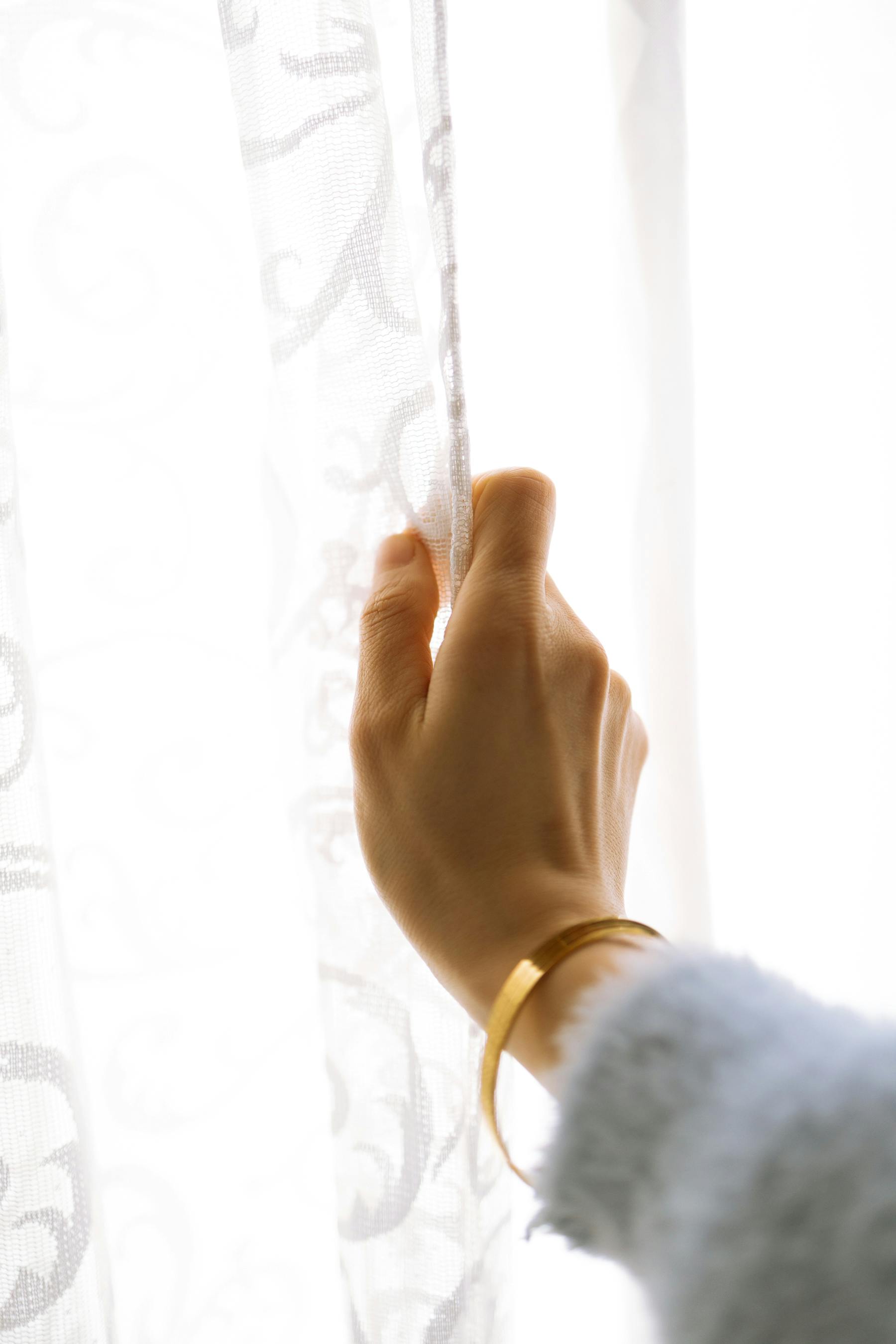Gratis En hånd med et armbånd som forsiktig berører et gjennomsiktig gardin, noe som vekker en følelse av ro og nysgjerrighet. Arkivbilde