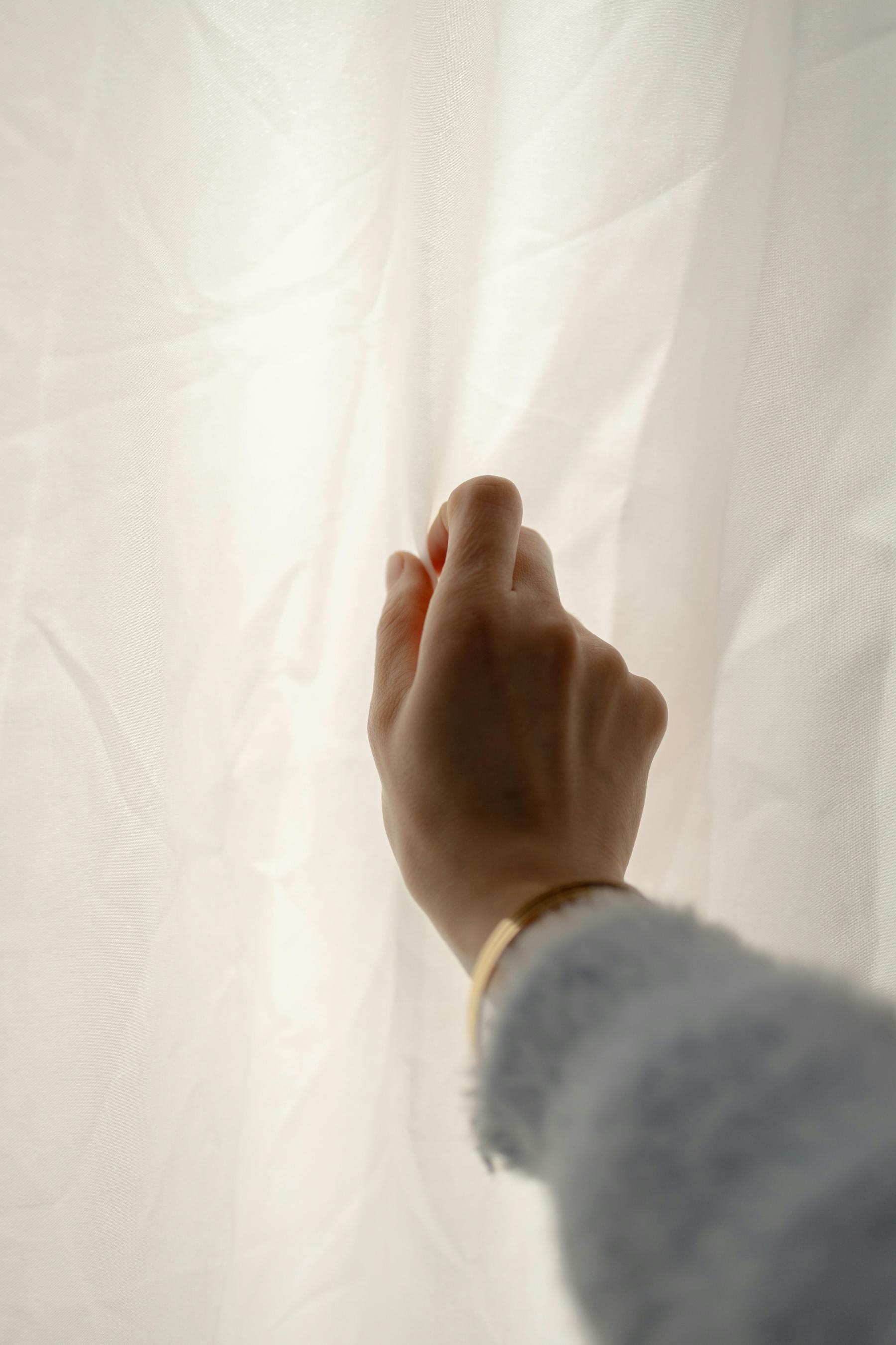 Free A hand gently lifts a white curtain, capturing a moment of calm and curiosity. Stock Photo
