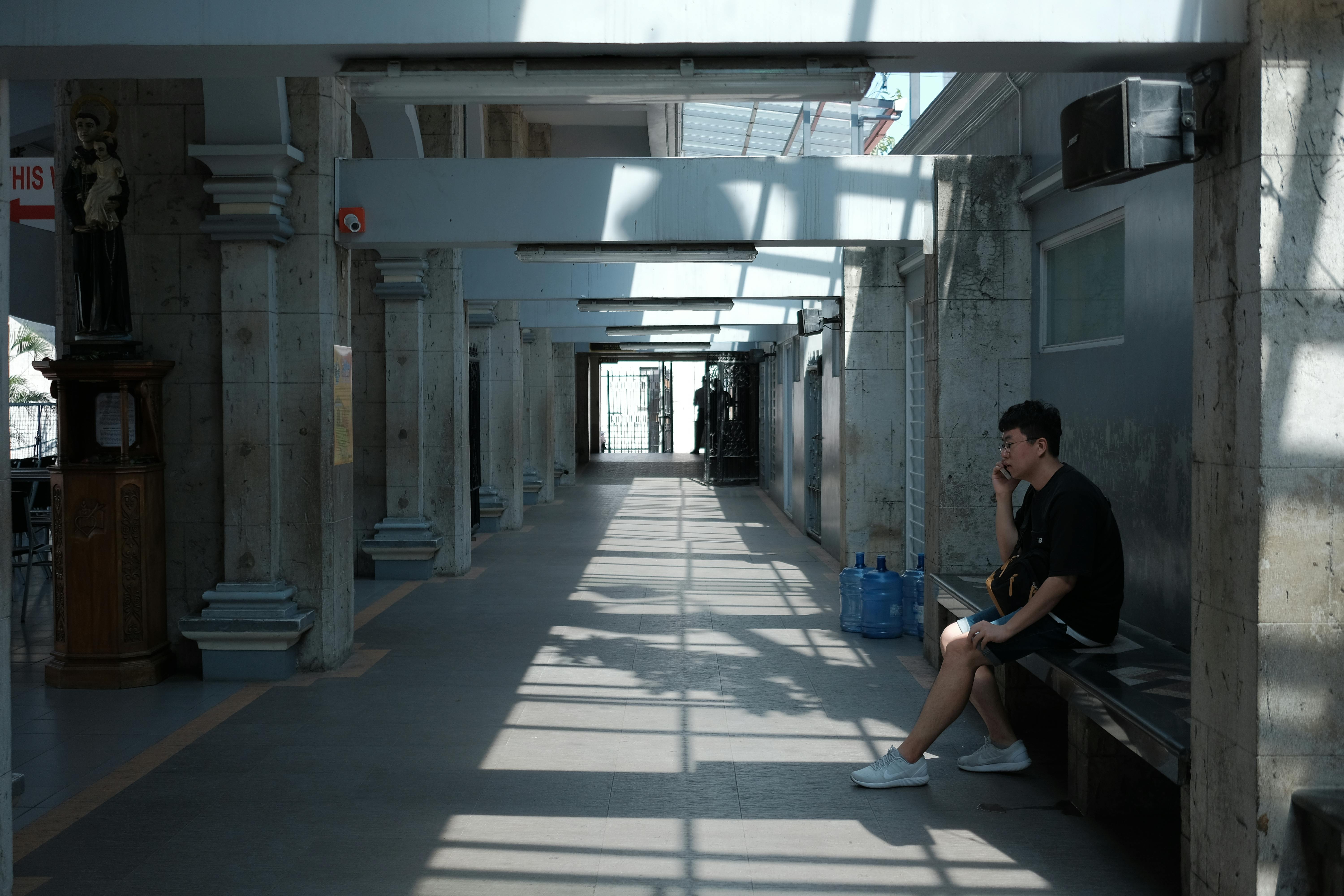 無料 中央ビサヤ地方の日当たりの良い廊下に、物思いにふけりながら座る男性。都会の風景。 写真素材