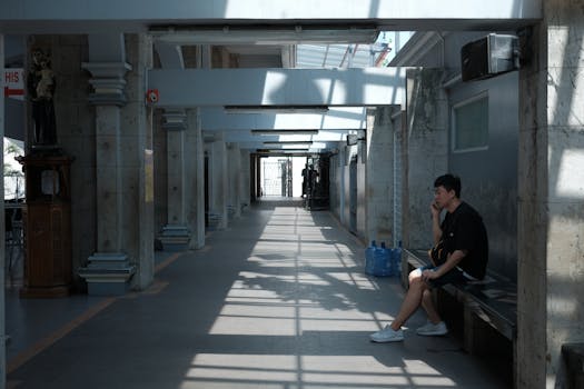 A man sits pensively in a sunny corridor in the Central Visayas. Urban setting.