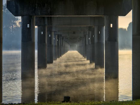 Serene view under a bridge in Galicia, Spain, with mist rising over the water.