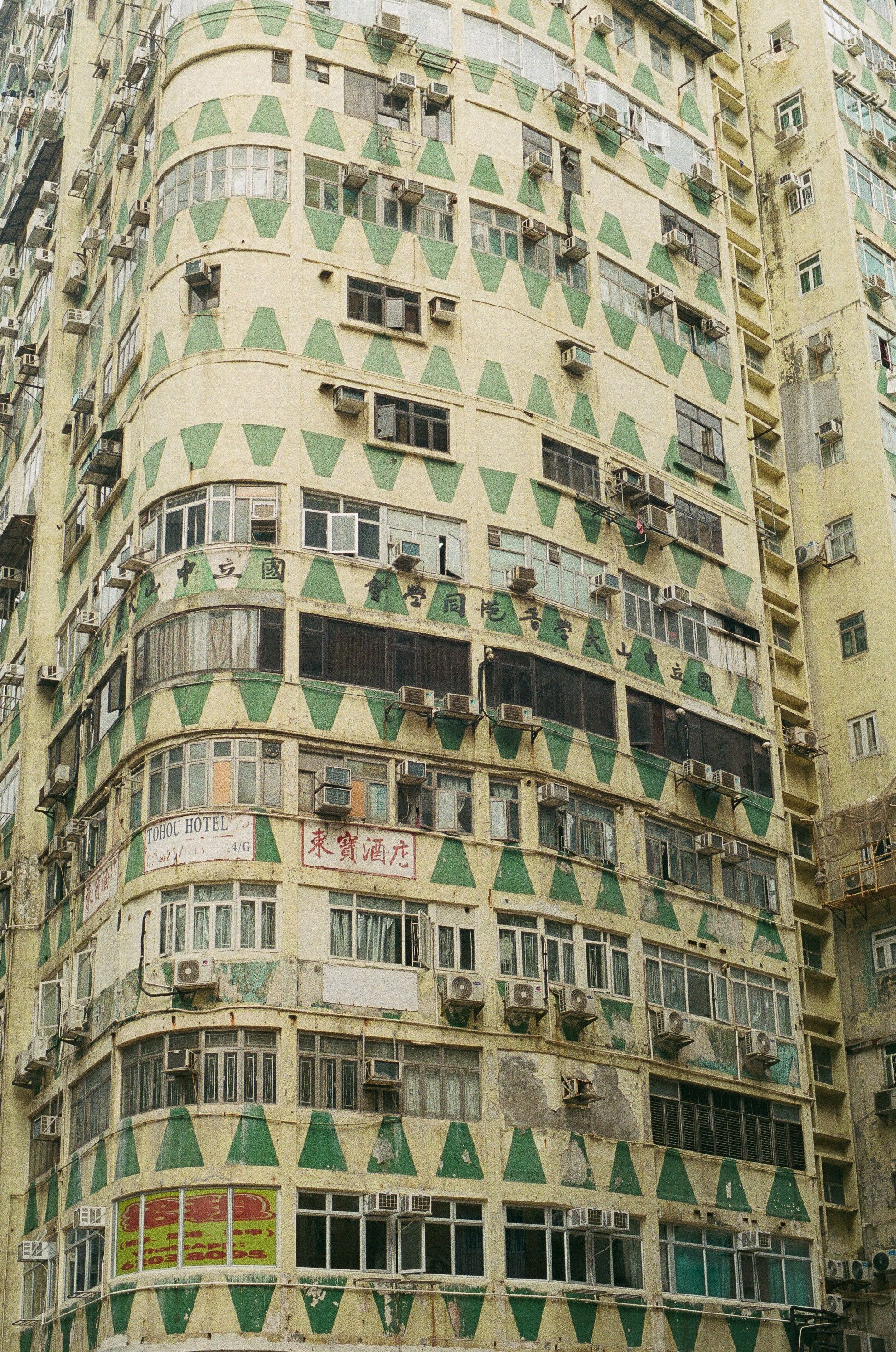 A tall urban residential building with a unique geometric facade featuring green patterns and air conditioning units.