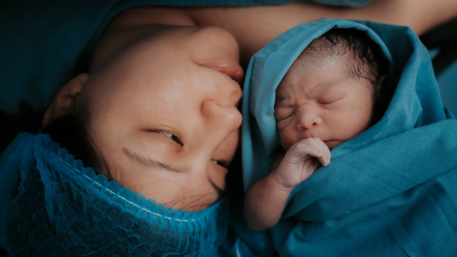 A touching image of a mother and her newborn baby wrapped in blue medical blankets.