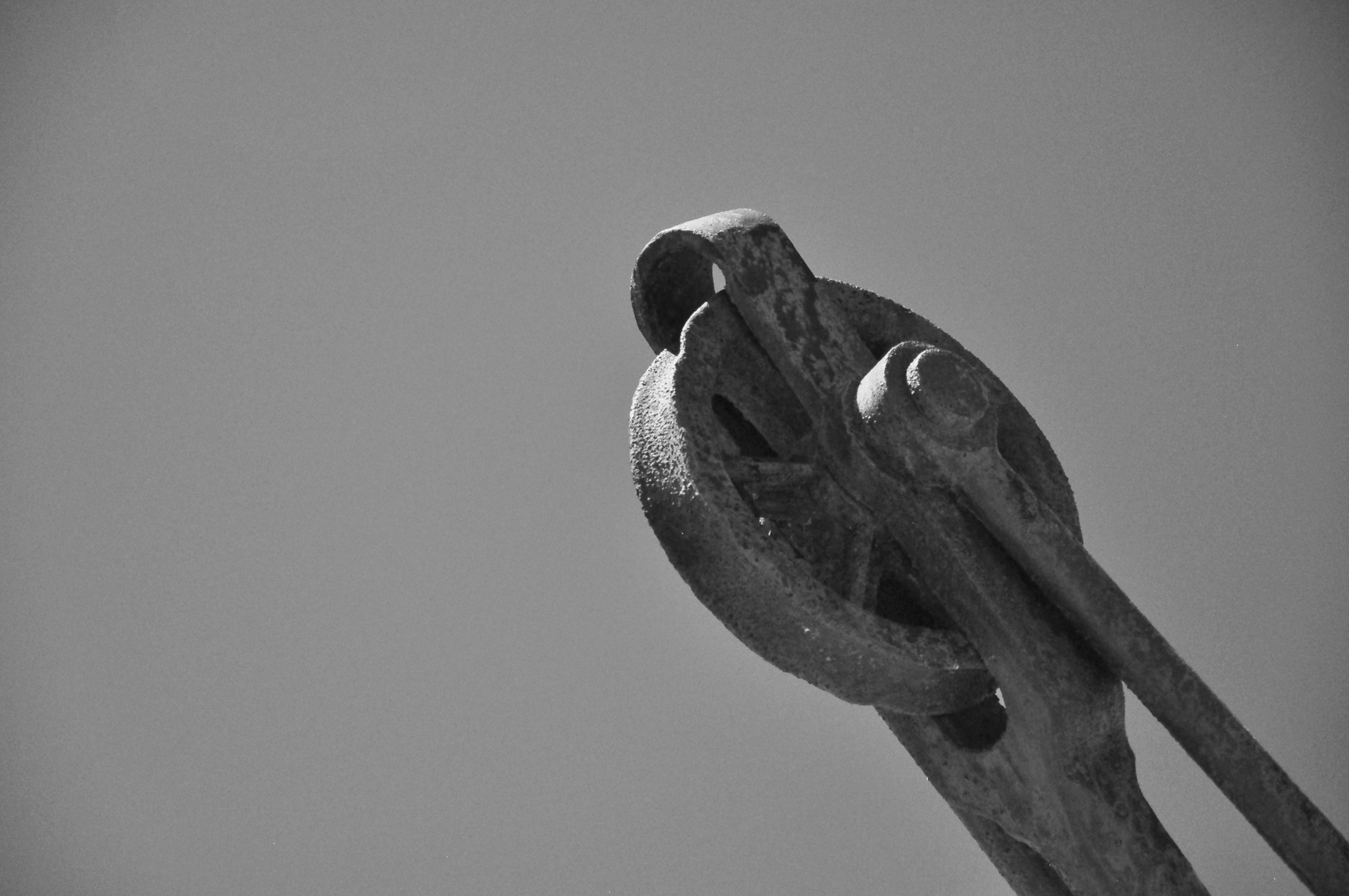 Gratis Primer plano de una polea industrial oxidada contra un cielo despejado, capturado en blanco y negro. Foto de stock