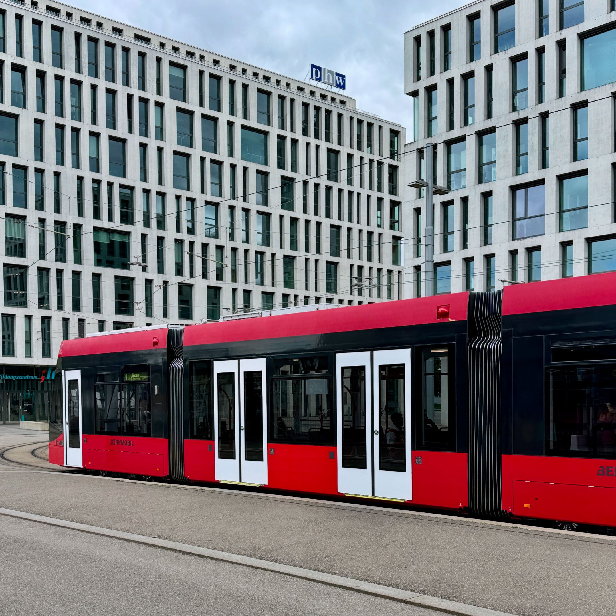 A sleek red tram passing through a modern urban area lined with office buildings.