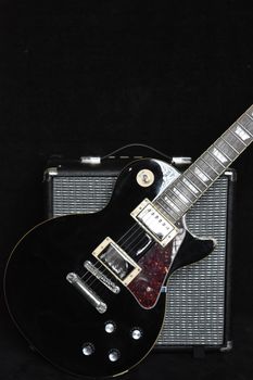 Close-up of a black electric guitar with amplifier on a dark background showcasing music gear.