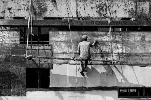 Worker on a scaffolding restores an old building facade in a dramatic black-and-white shot.