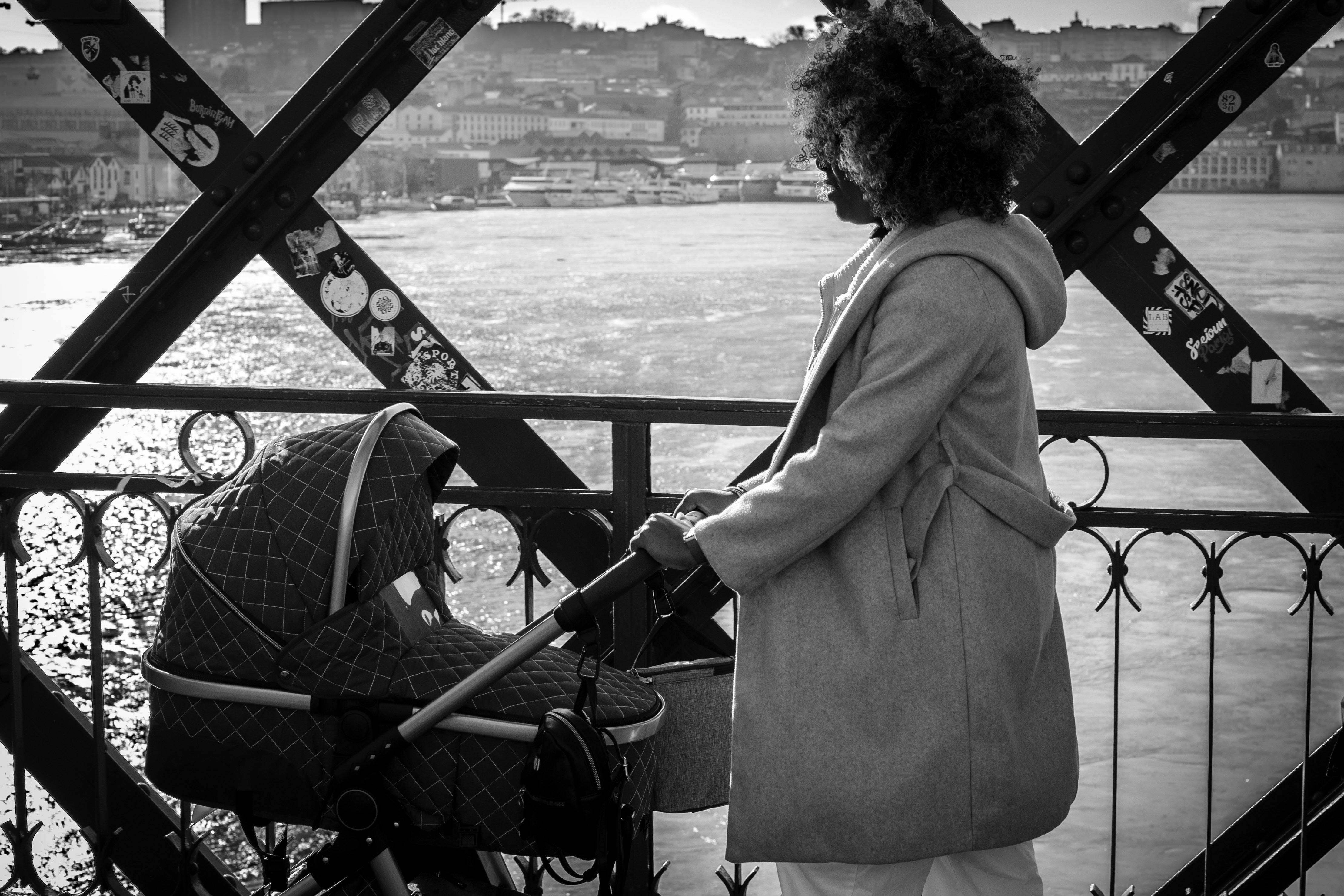 無料 ベビーカーを押して街の橋の上で美しい景色を楽しんでいる女性の白黒写真。 写真素材