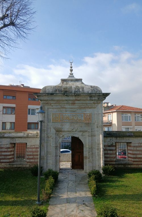 Free A historic stone archway featuring intricate carvings set against a clear blue sky with urban backdrop. Stock Photo