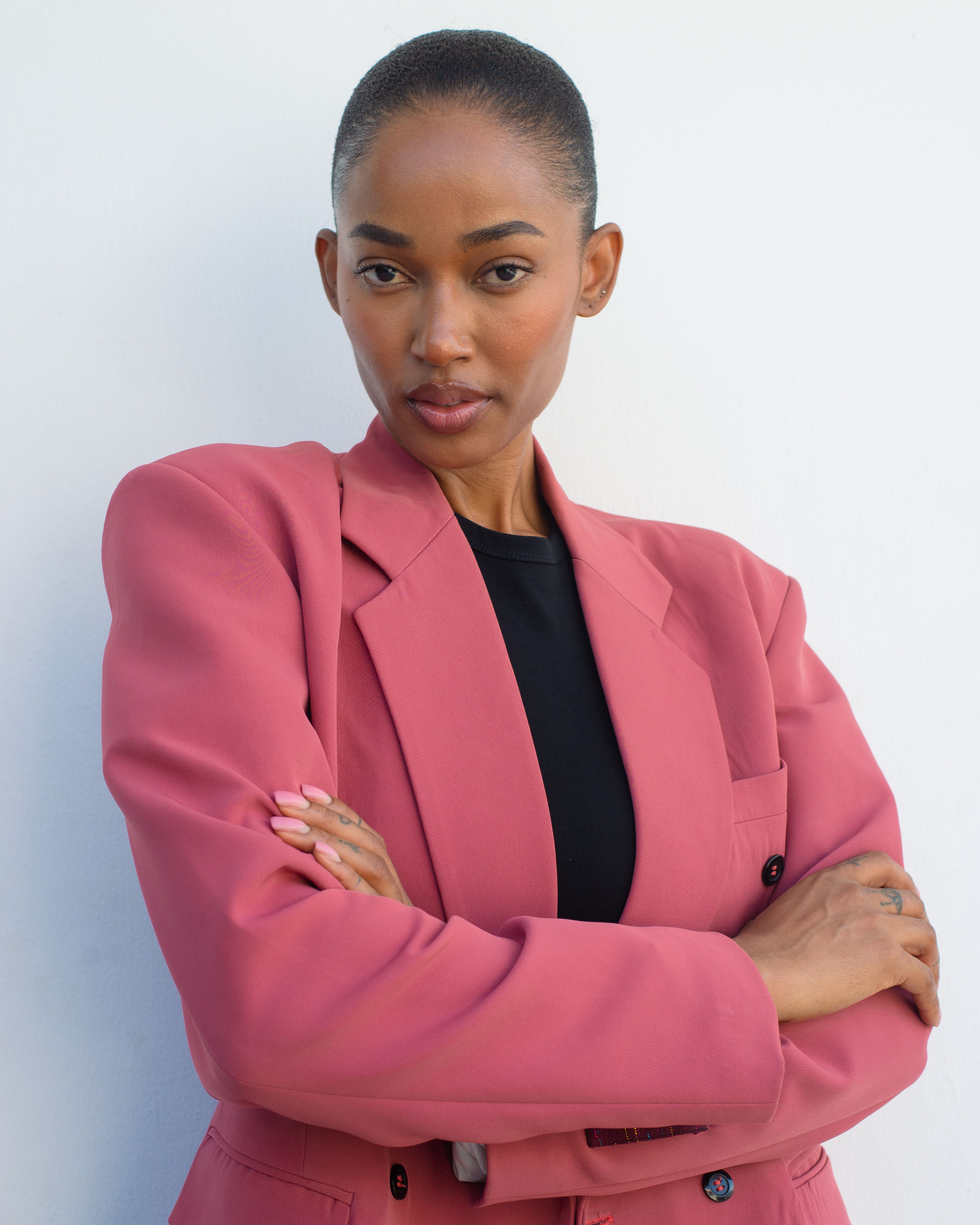 Striking portrait of a confident woman in a pink blazer against a plain background.