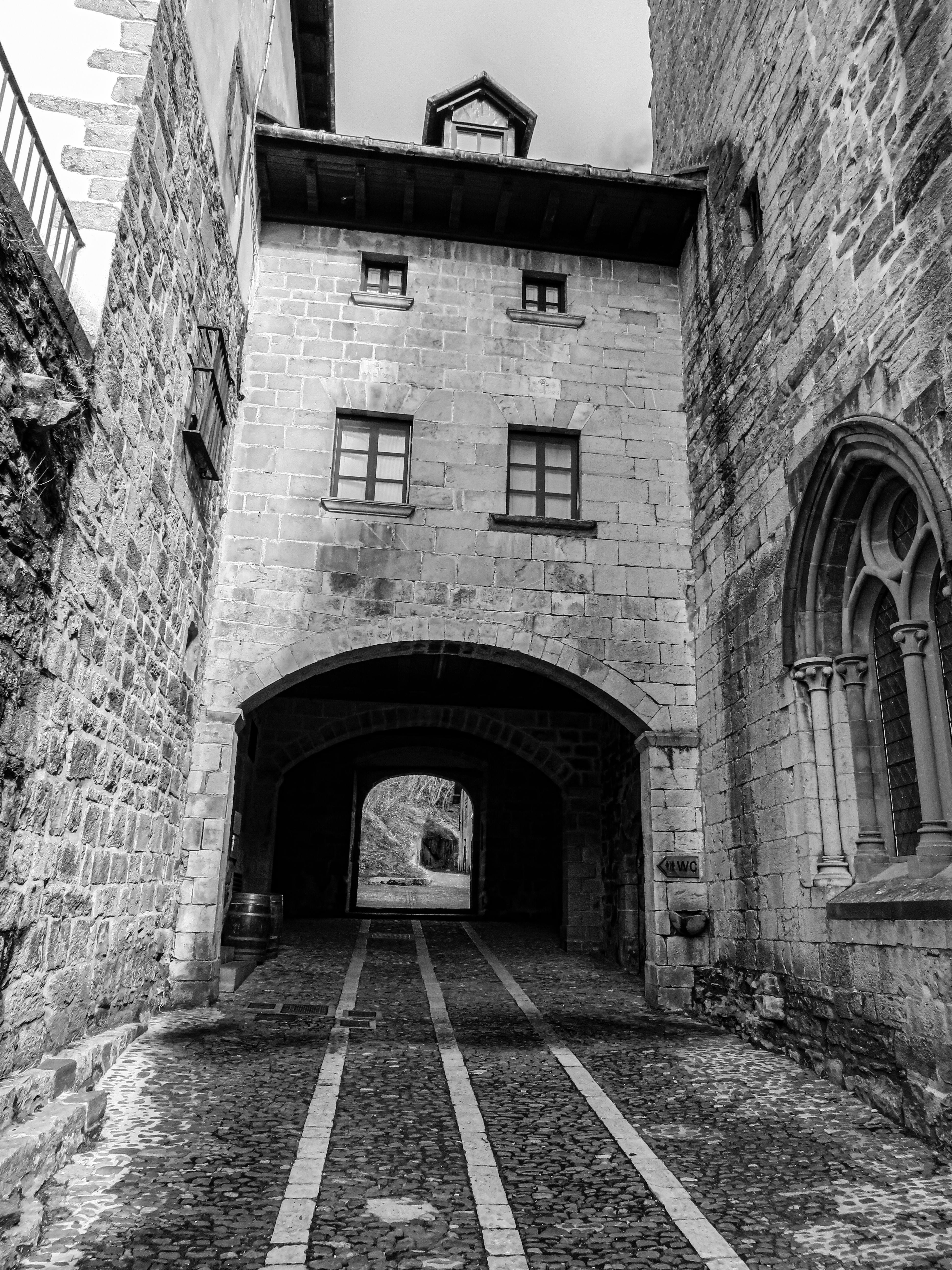 бесплатная На этой черно-белой фотографии вы увидите историческую каменную арку, ведущую в средневековую деревню. Стоковое фото