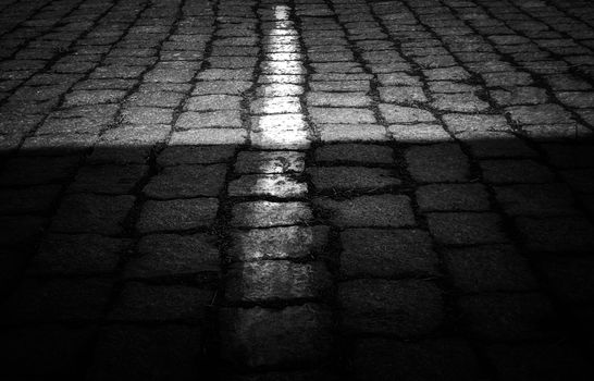 Moody black and white photo of cobblestone pavement with dramatic lighting contrast.