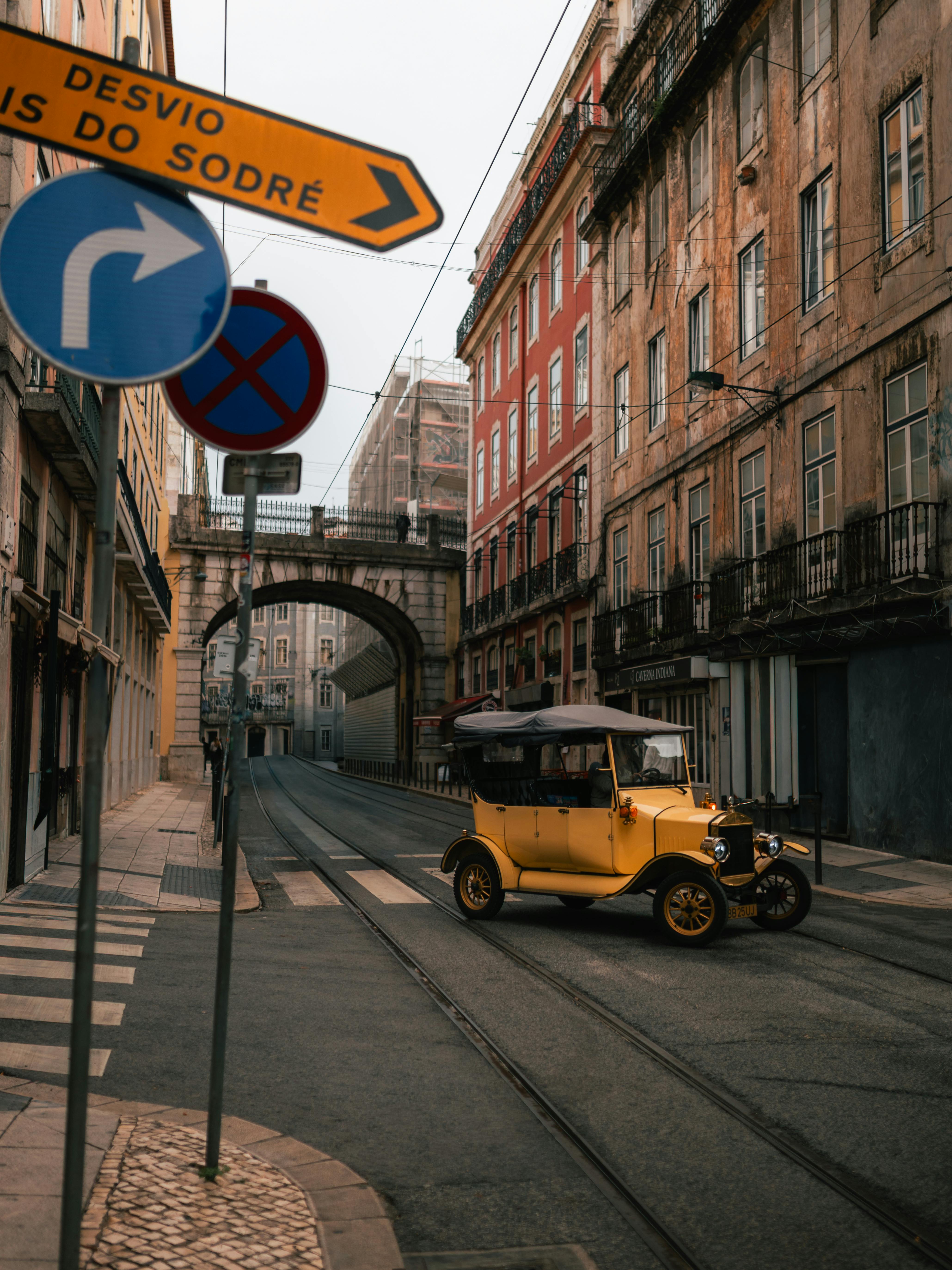 無料 歴史的な建築物と交通標識のある静かなリスボンの通りに停まっている黄色いビンテージ車。 写真素材
