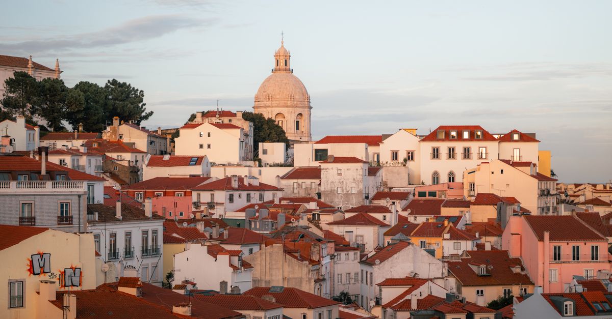 A picturesque view of Lisbon's historic Alfama district, showcasing traditional buildings and the iconic dome under a sunset sky.