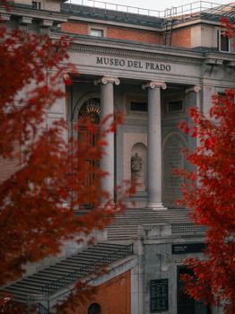 Stunning autumn view of Museo del Prado in Madrid framed by vibrant red leaves.