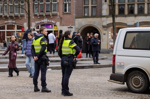 Free City square scene with Dutch police officers on patrol, surrounded by pedestrians and a police vehicle. Stock Photo