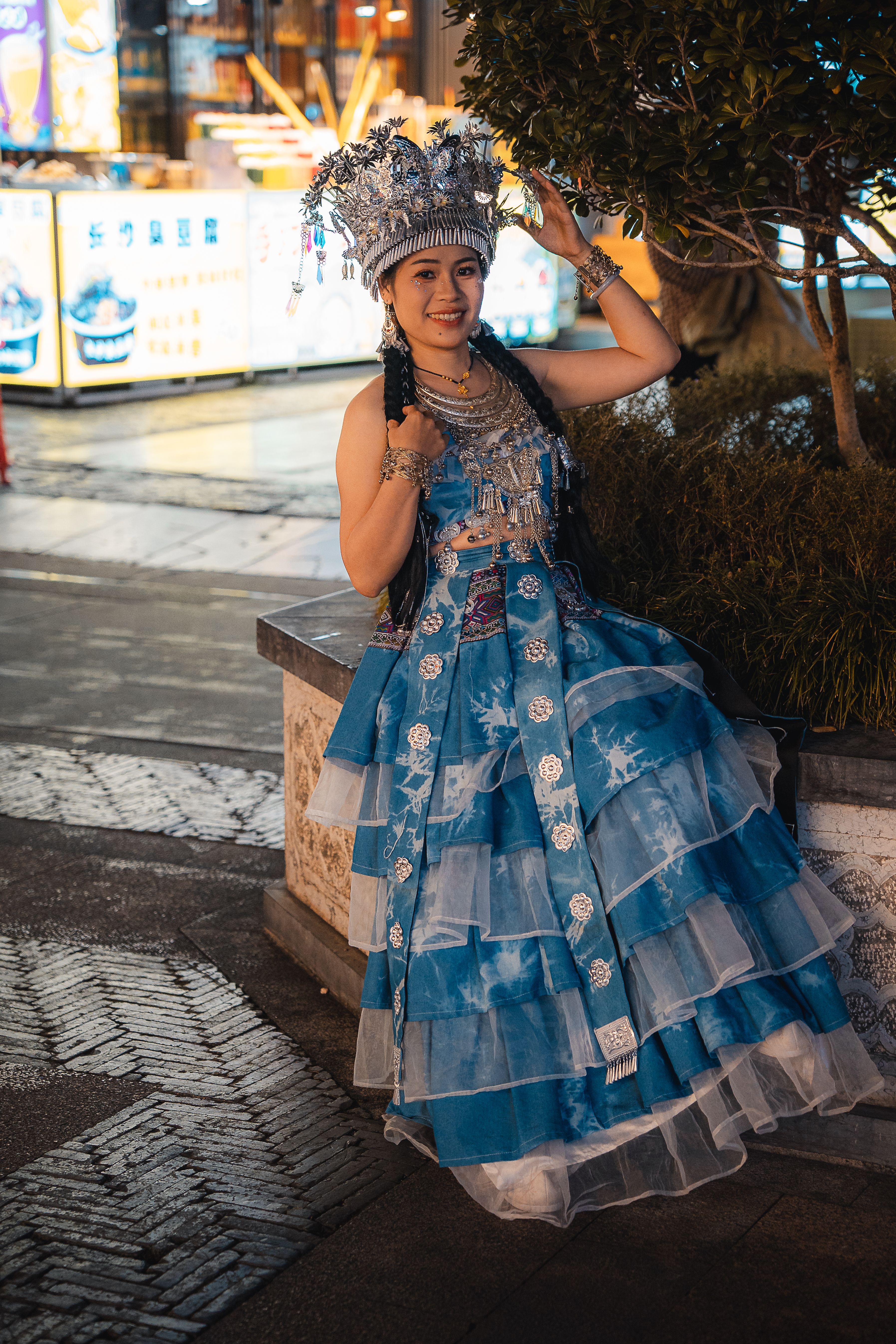 Woman in traditional Miao attire poses at night in Guilin, China, showcasing cultural attire.
