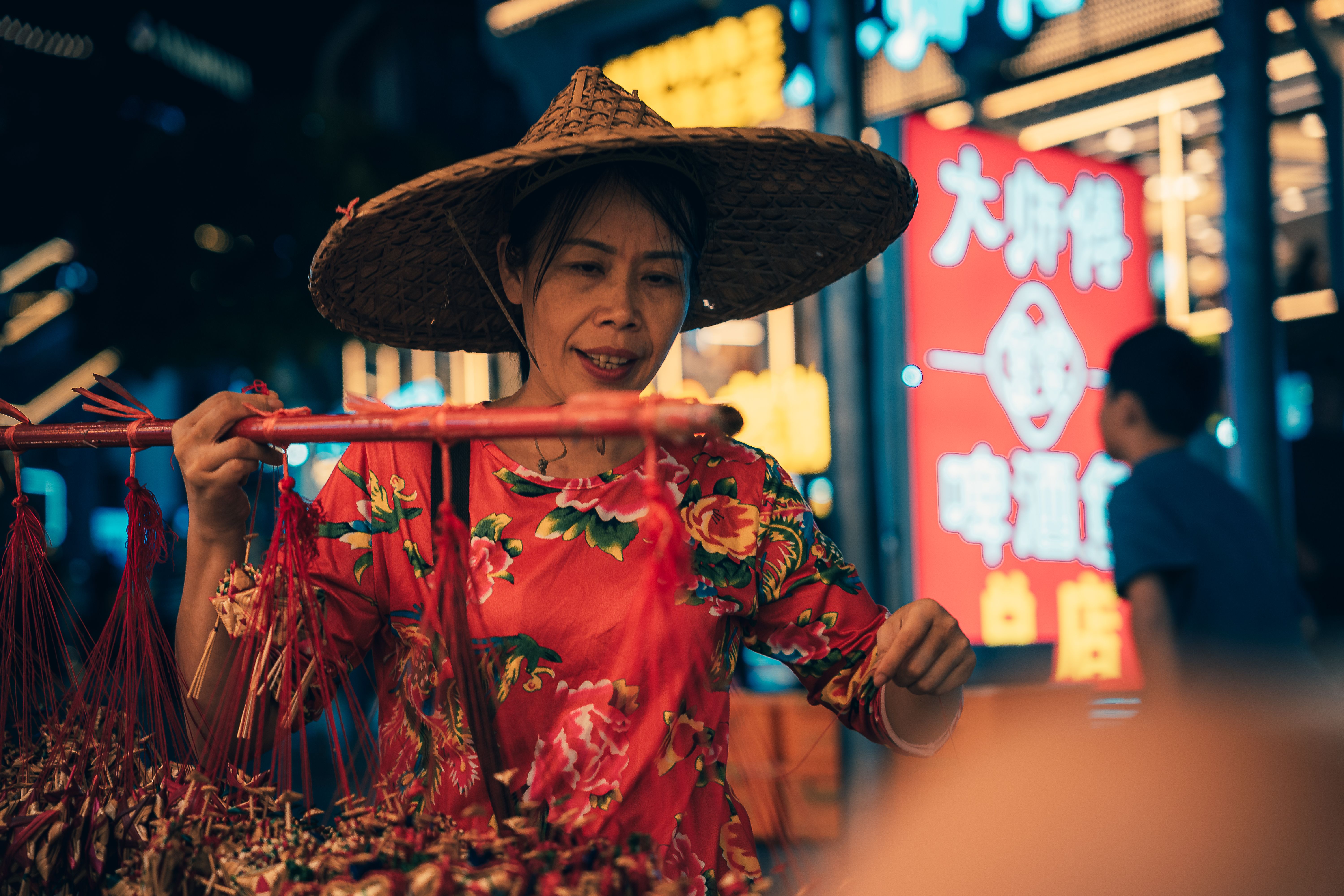 Woman vendor in Guilin night market wearing a straw hat, displaying handcrafted items.