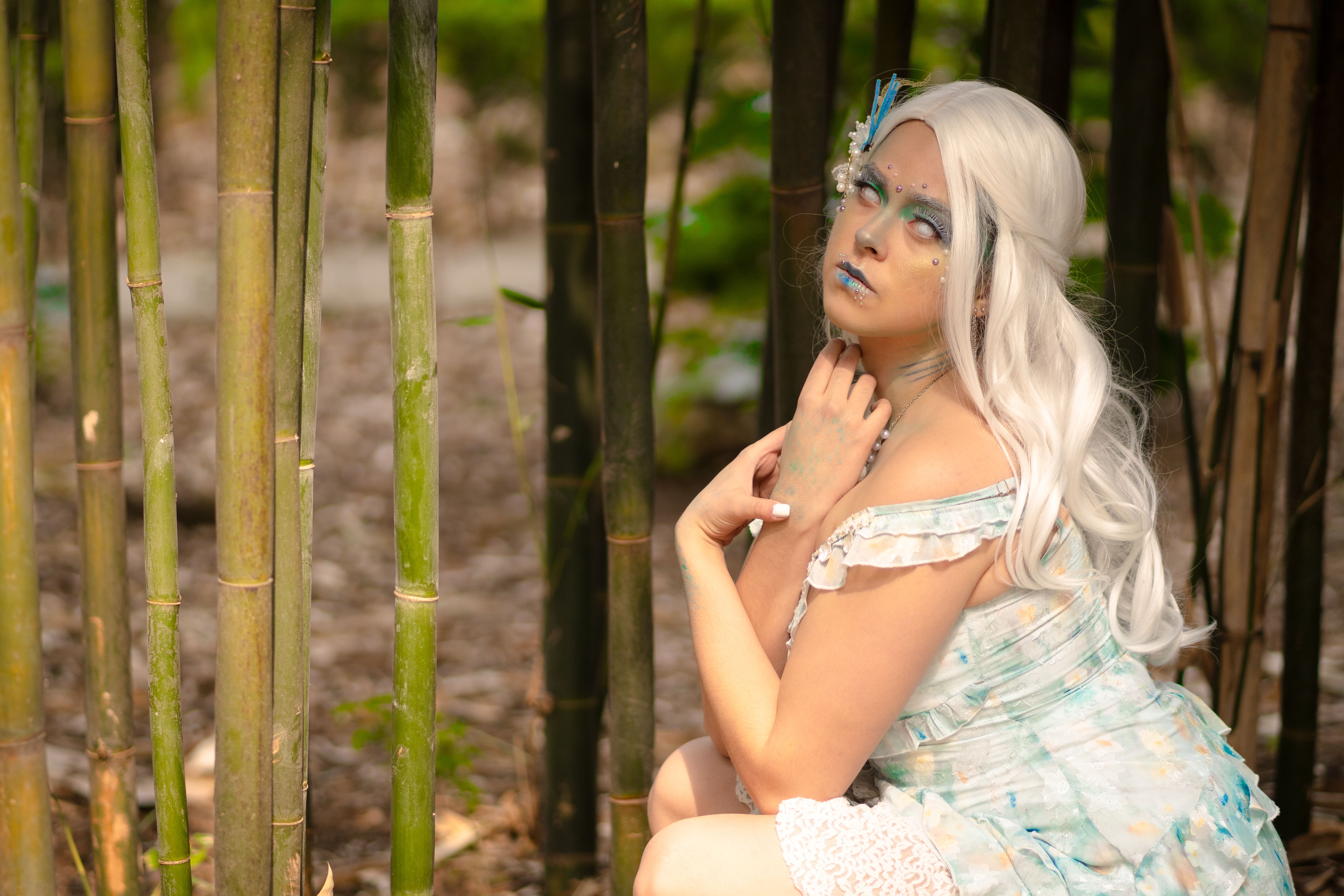 A woman in an artistic costume with fantasy makeup poses in a bamboo grove.