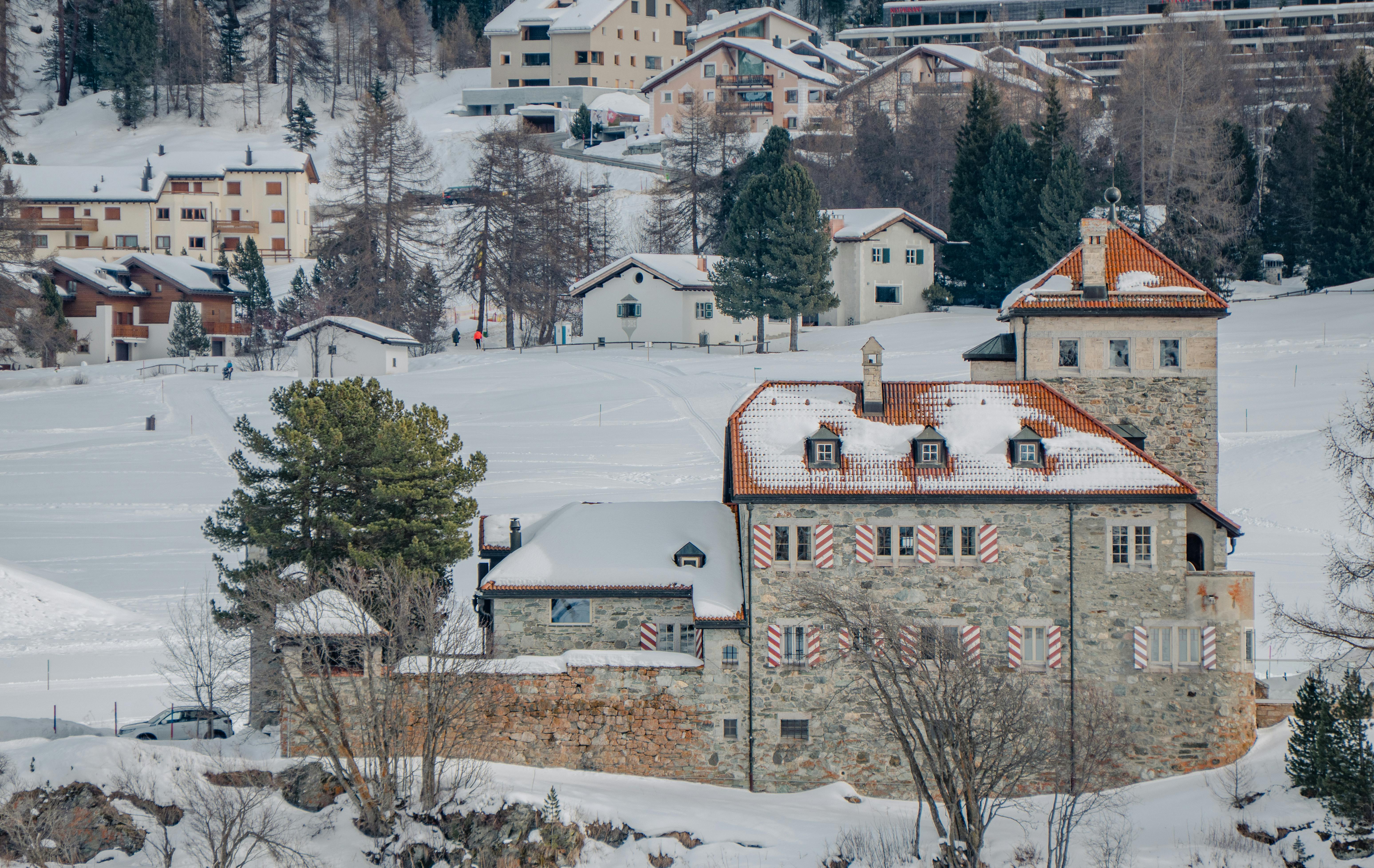 бесплатная Живописный зимний пейзаж заснеженной деревни, расположенной в швейцарских Альпах, с элементами традиционной архитектуры. Стоковое фото