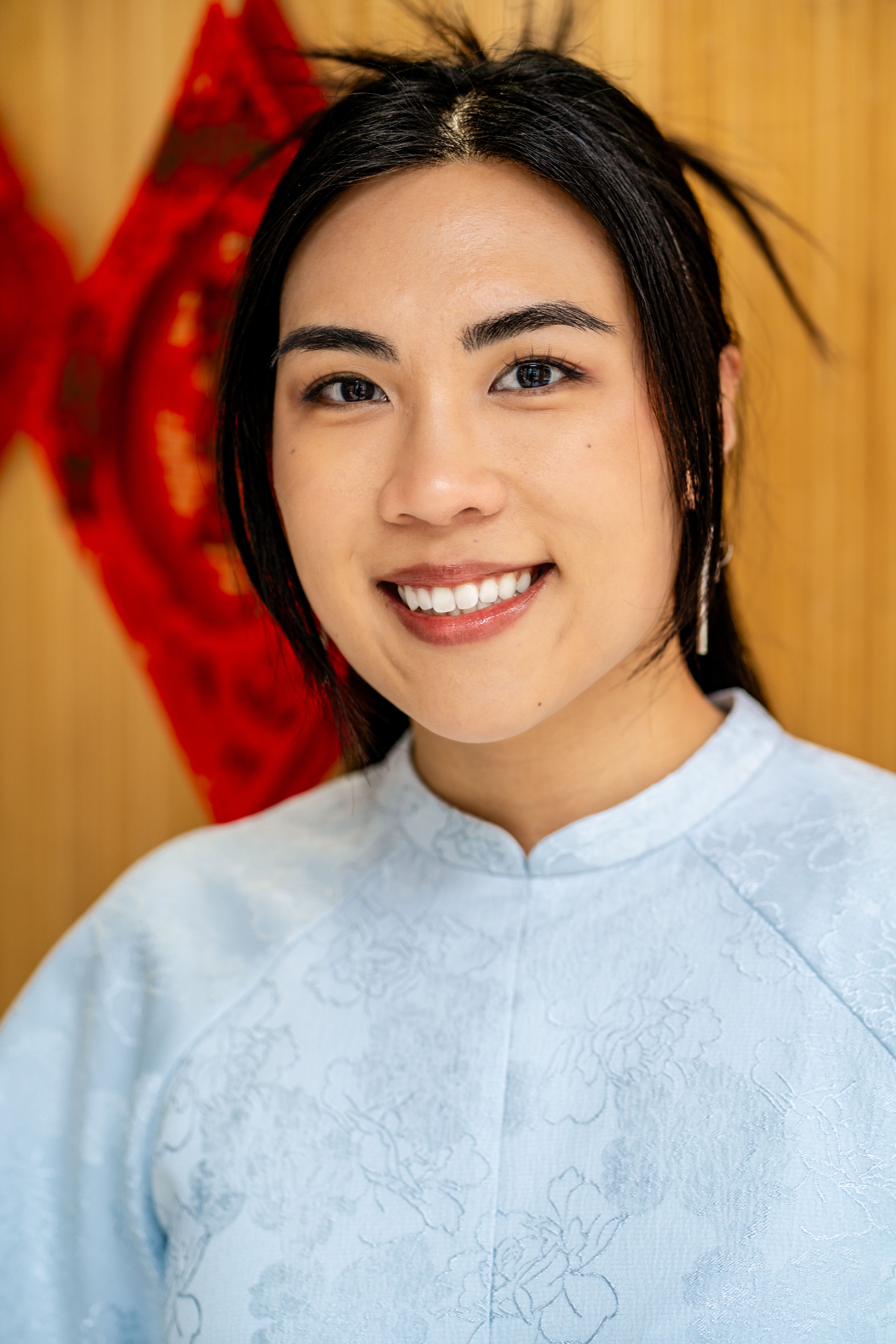 A cheerful woman in blue traditional attire poses indoors. Lunar New Year theme.