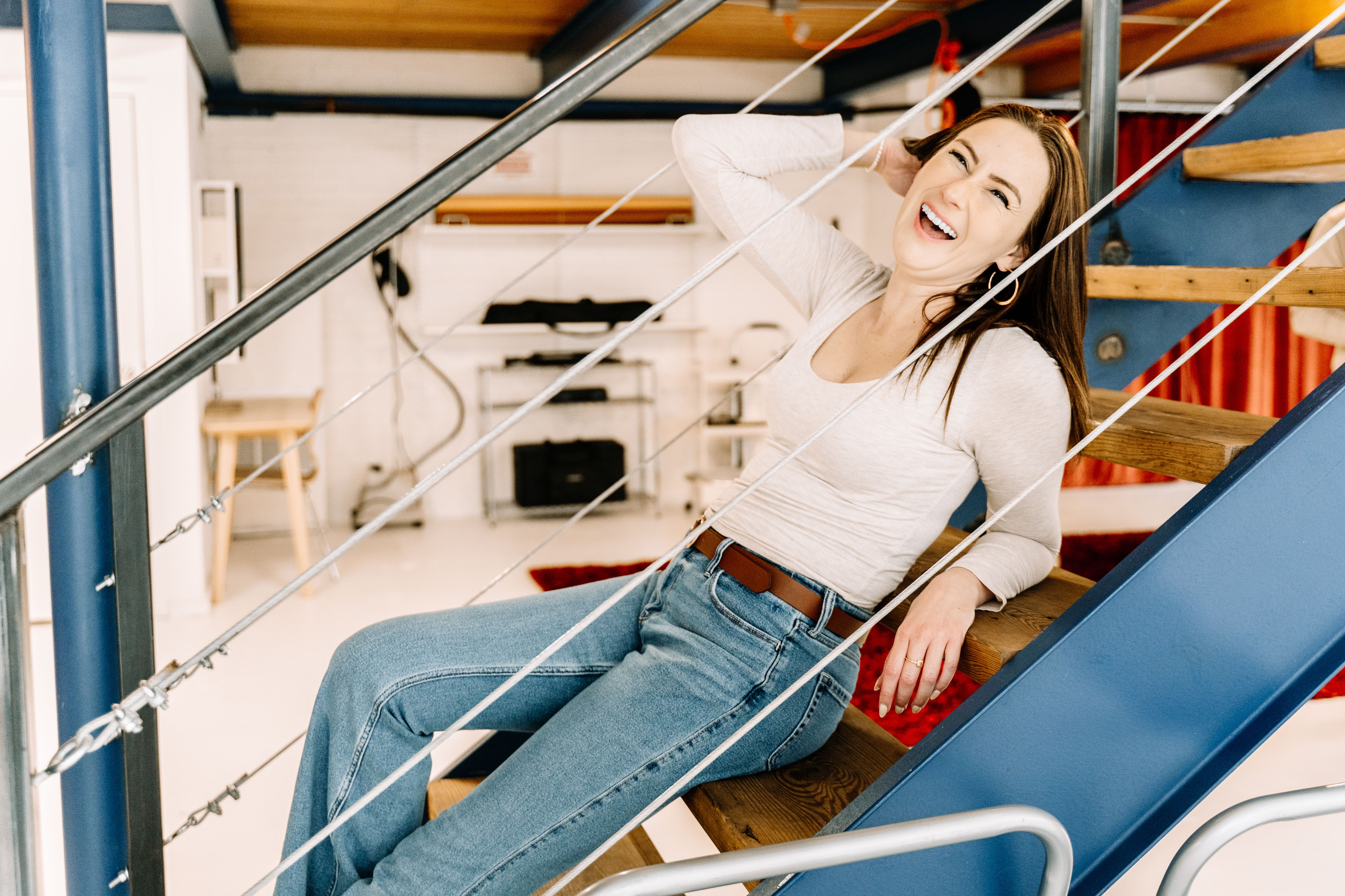 A cheerful woman laughing and reclining on a stylish indoor staircase in a modern studio setting.