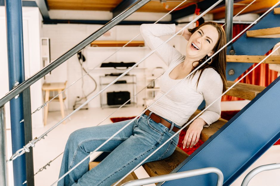 A cheerful woman laughing and reclining on a stylish indoor staircase in a modern studio setting. A cheerful woman laughing and reclining on a stylish indoor staircase in a modern studio setting.