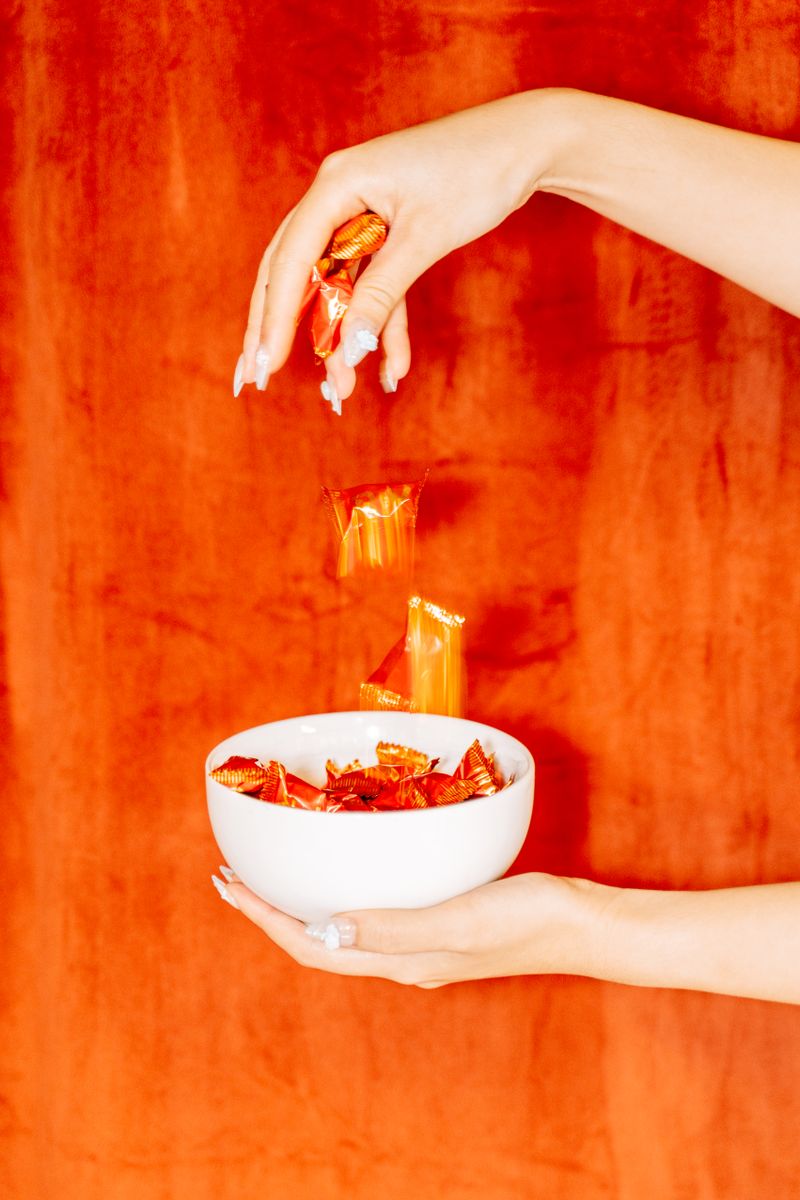 Hands pouring wrapped candy pieces into a bowl at StyliqHome Candy Cupboard