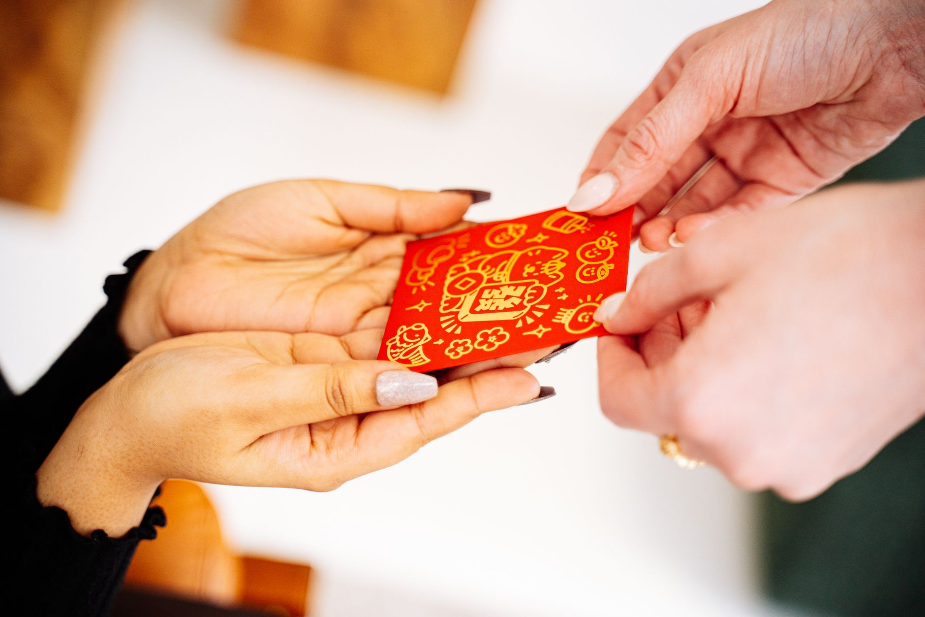 Hands exchanging a decorative red envelope for Lunar New Year, symbolizing good luck and prosperity.