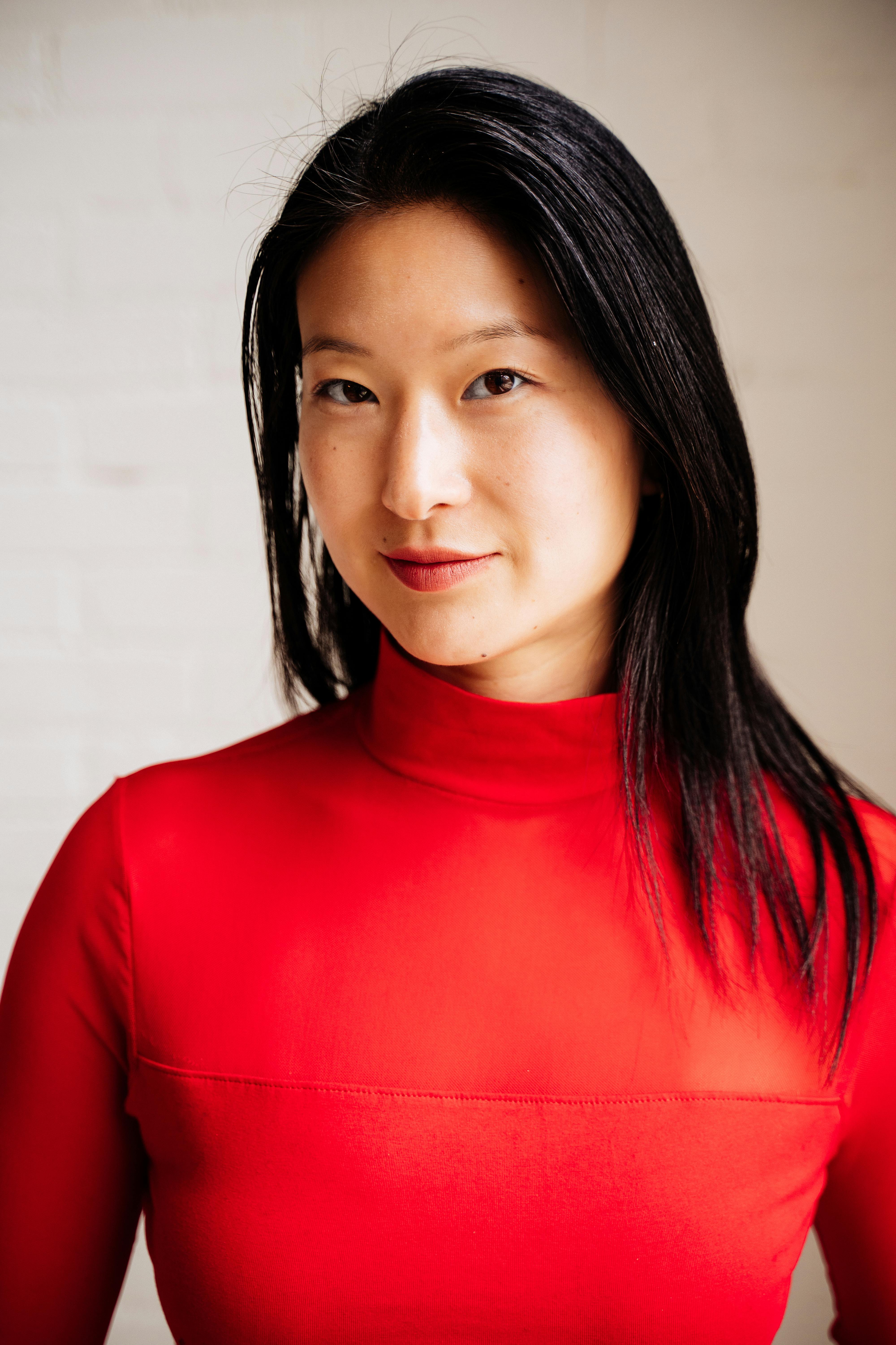 Studio portrait of an east Asian woman in a vivid red top, conveying confidence and style.