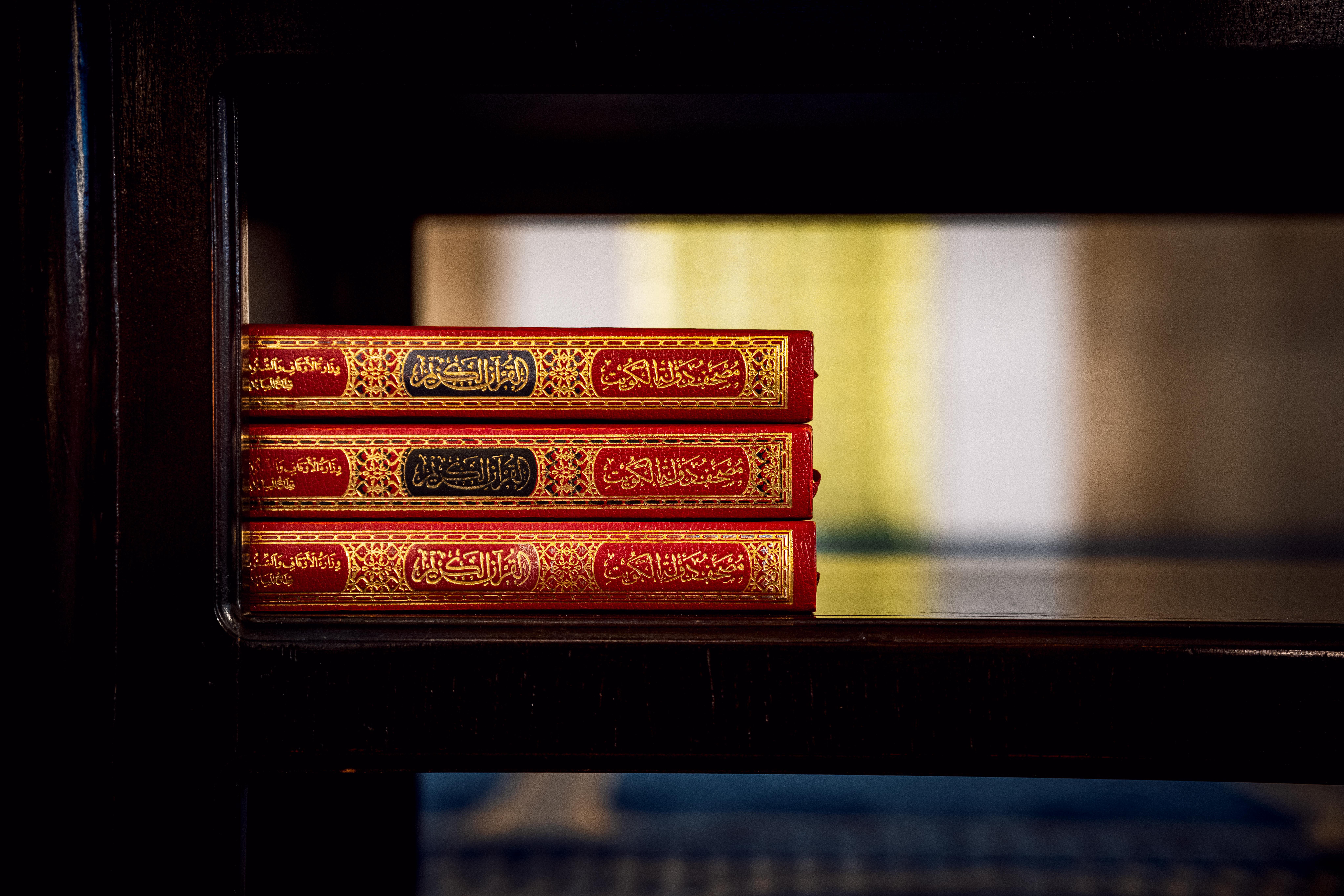 бесплатная Три Корана в богато украшенных обложках выставлены на деревянной полке внутри мечети, демонстрируя элементы исламской культуры. Стоковое фото