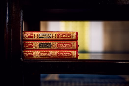 Three Qurans with ornate covers displayed on a wooden shelf inside a mosque, highlighting Islamic culture.