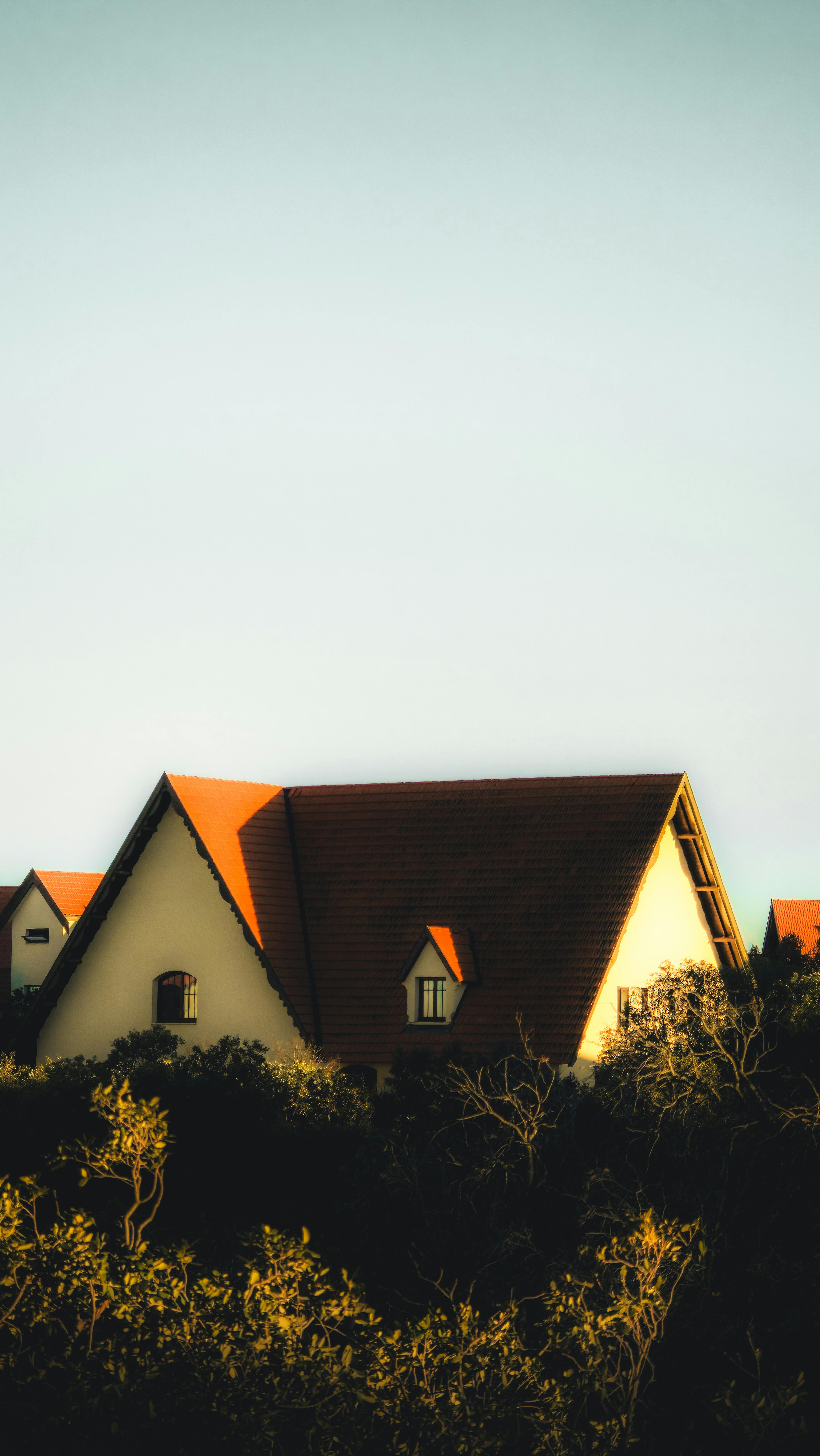 Free A picturesque cottage with a red roof surrounded by lush greenery, captured at sunset. Stock Photo