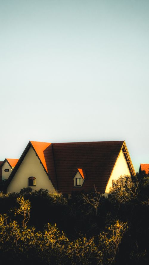 Free A picturesque cottage with a red roof surrounded by lush greenery, captured at sunset. Stock Photo