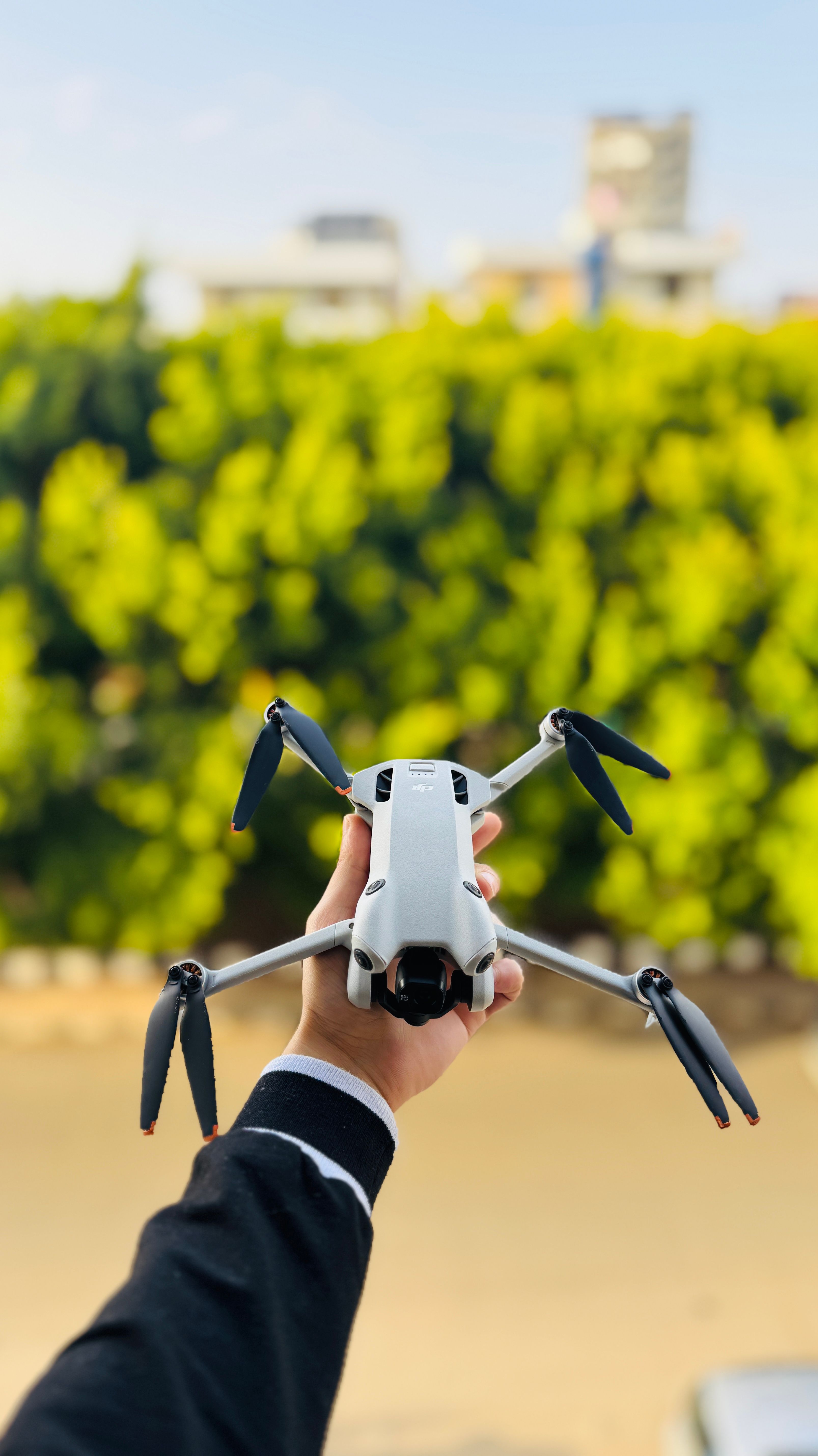 A hand holding a drone against a backdrop of vibrant green foliage in Tartus, Syria.
