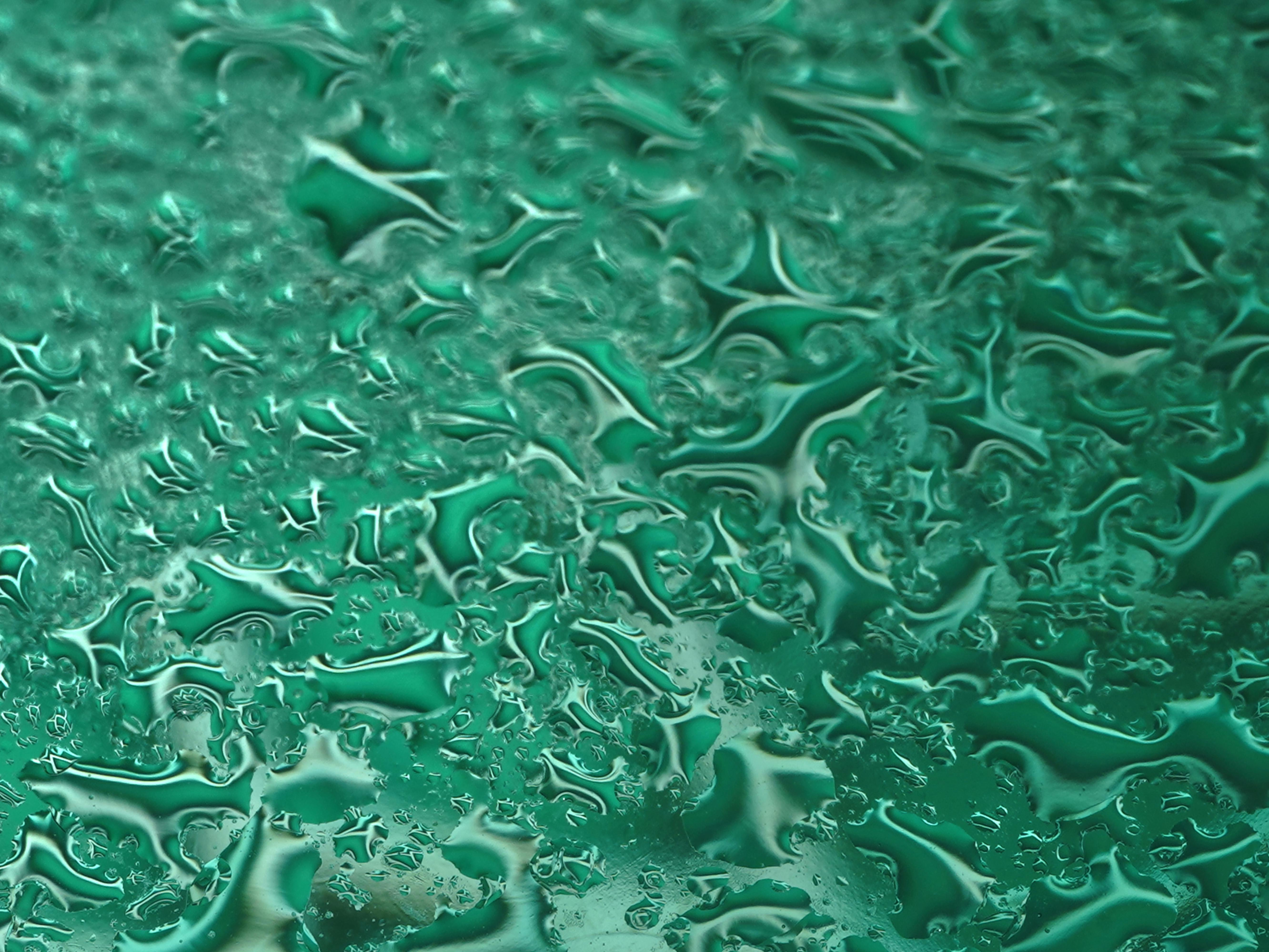 бесплатная Крупный план абстрактных узоров, образованных зелеными каплями воды на стекле. Стоковое фото