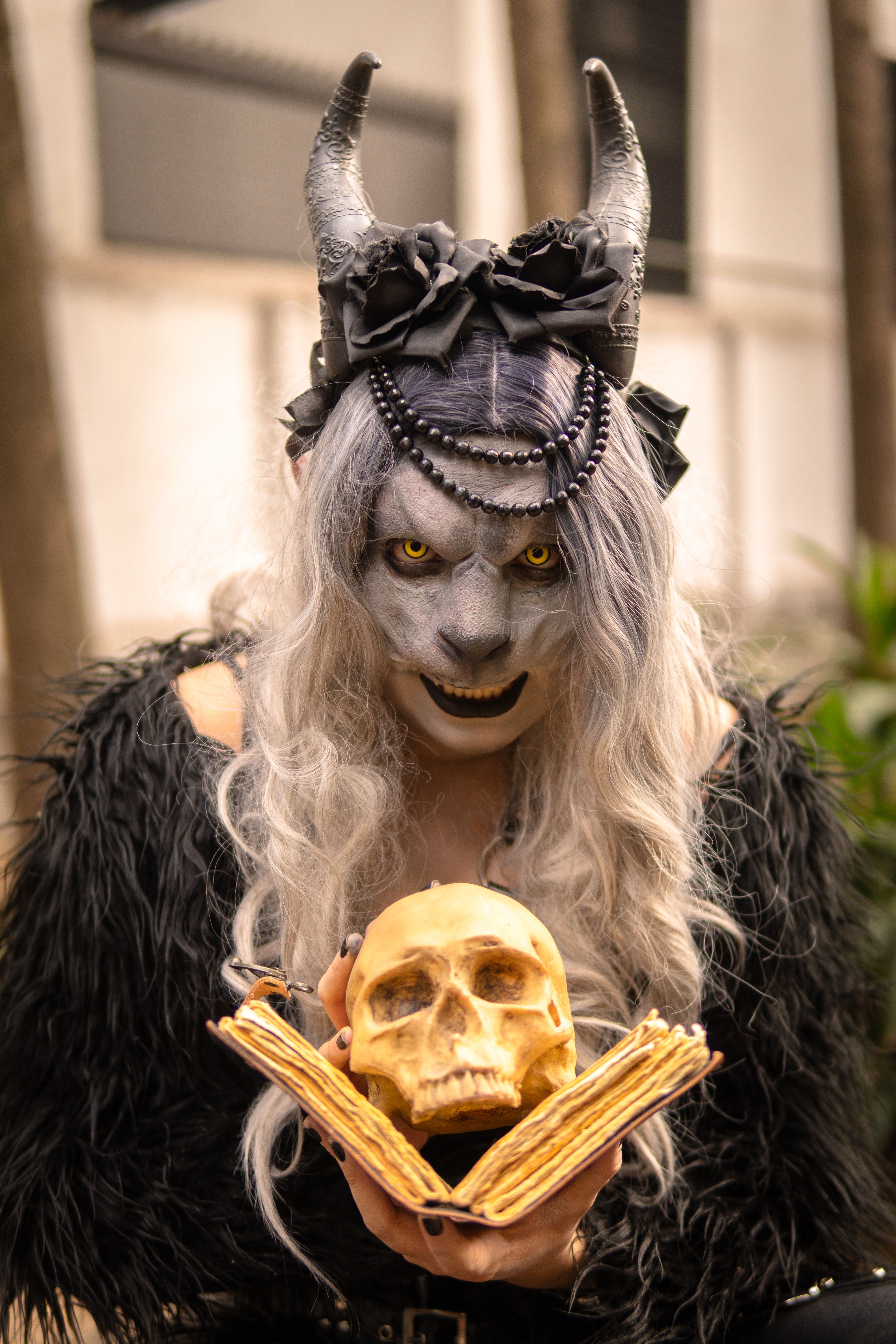 Fantasy character in a dark costume holding a skull in a Mexican street setting.