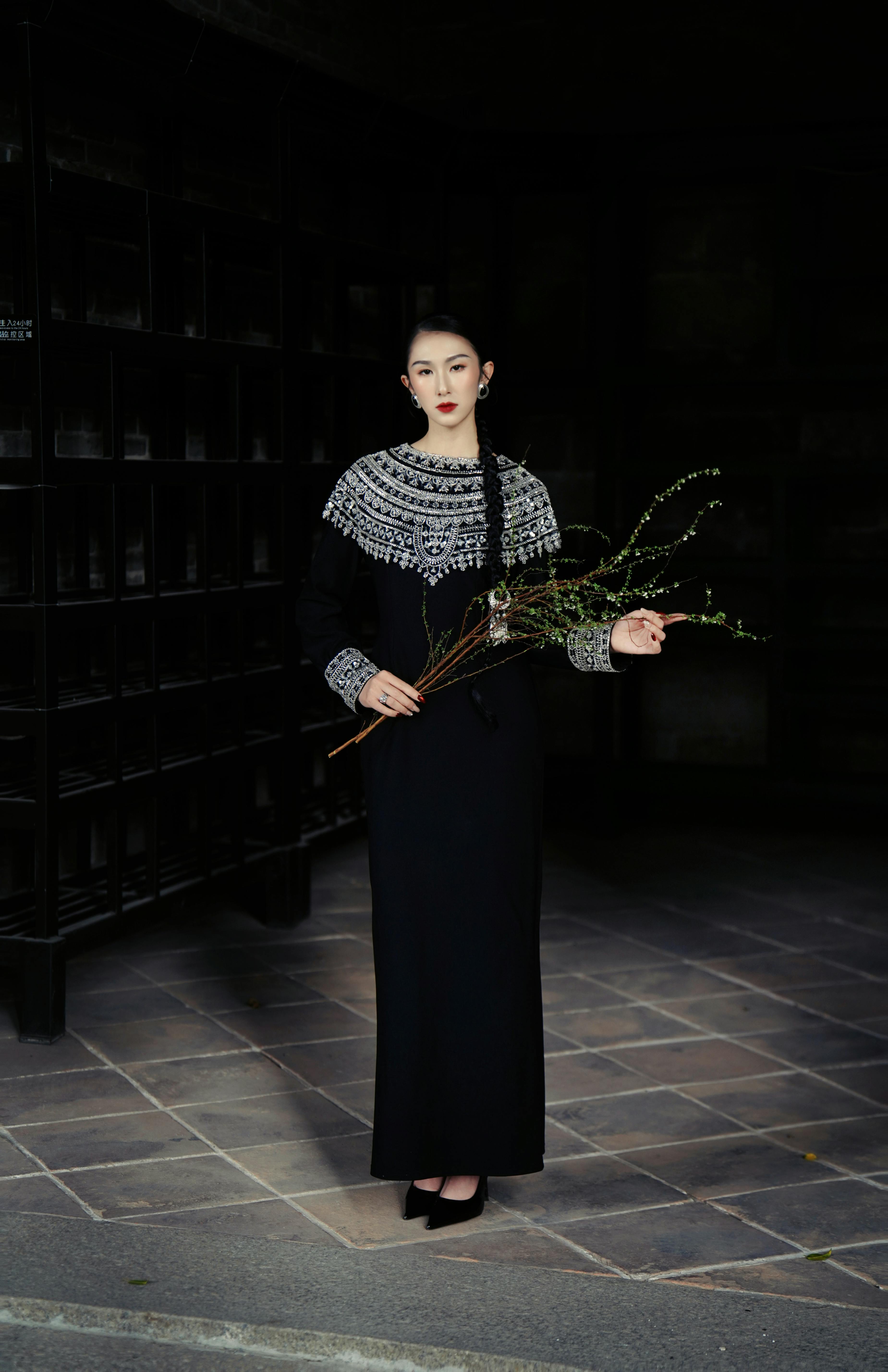 бесплатная Портрет элегантной женщины в шикарном черном платье, держащей ветки в помещении. Стоковое фото