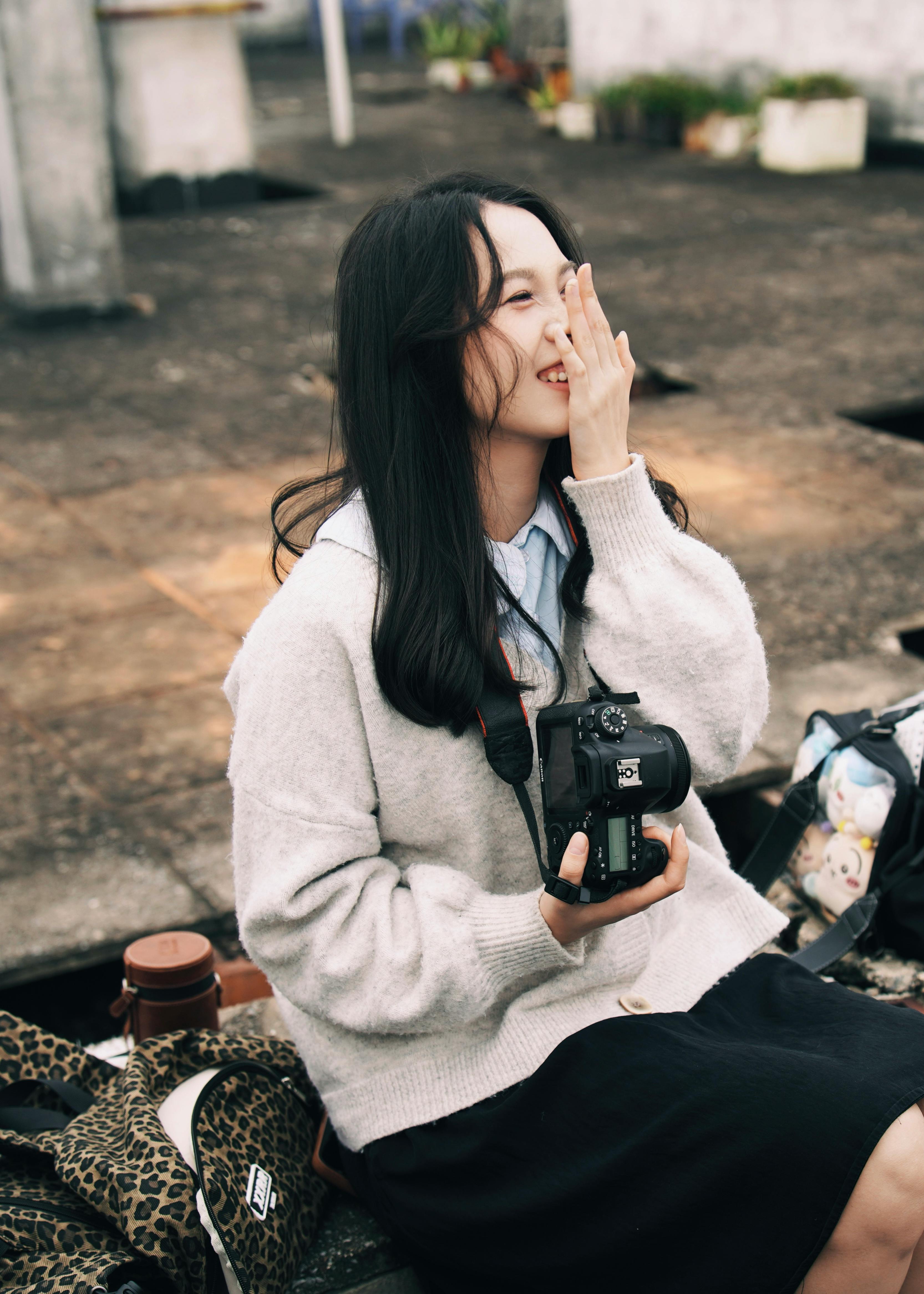 Free Smiling young woman with DSLR camera sitting outdoors, enjoying photography. Stock Photo