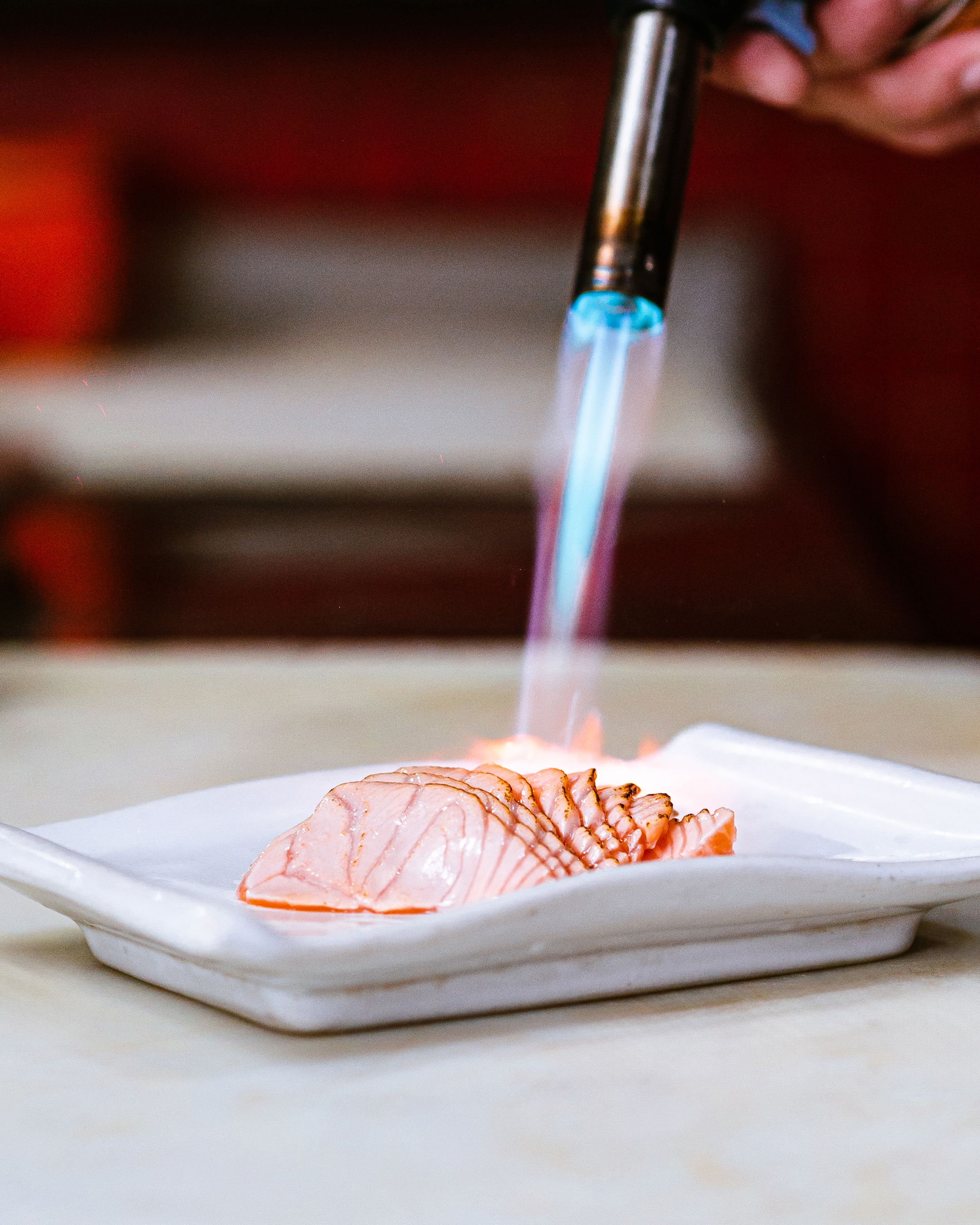Elegant preparation of salmon sashimi with a blowtorch, highlighting culinary artistry.