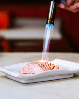 Elegant preparation of salmon sashimi with a blowtorch, highlighting culinary artistry.