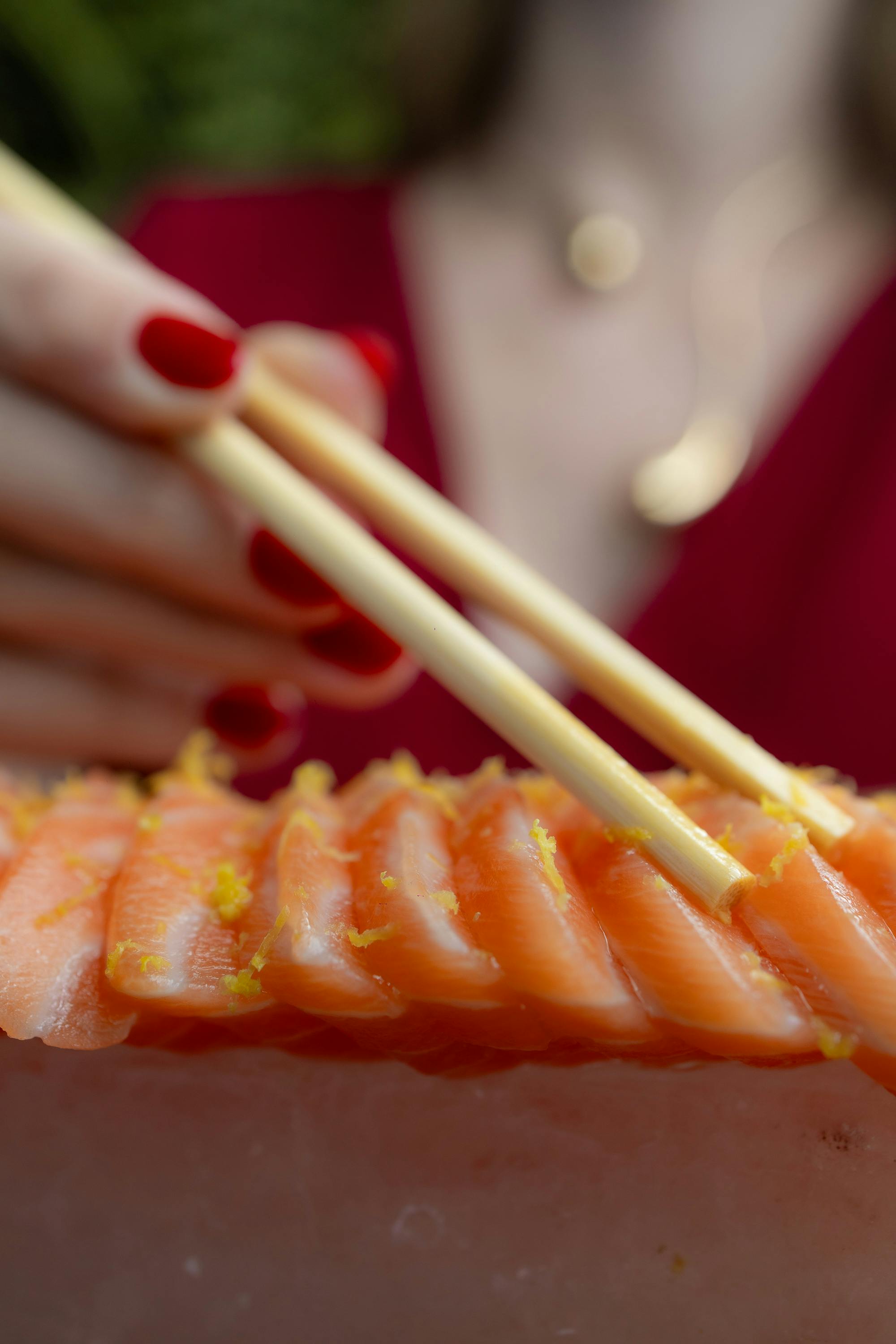 Gratis Foto makro sashimi salmon segar dengan sumpit, dihiasi dengan parutan kulit jeruk untuk presentasi yang menarik. Foto Stok