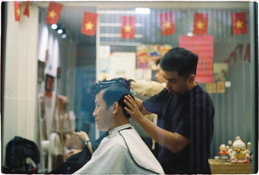 Barber giving a haircut in a Vietnamese barbershop with flags overhead.