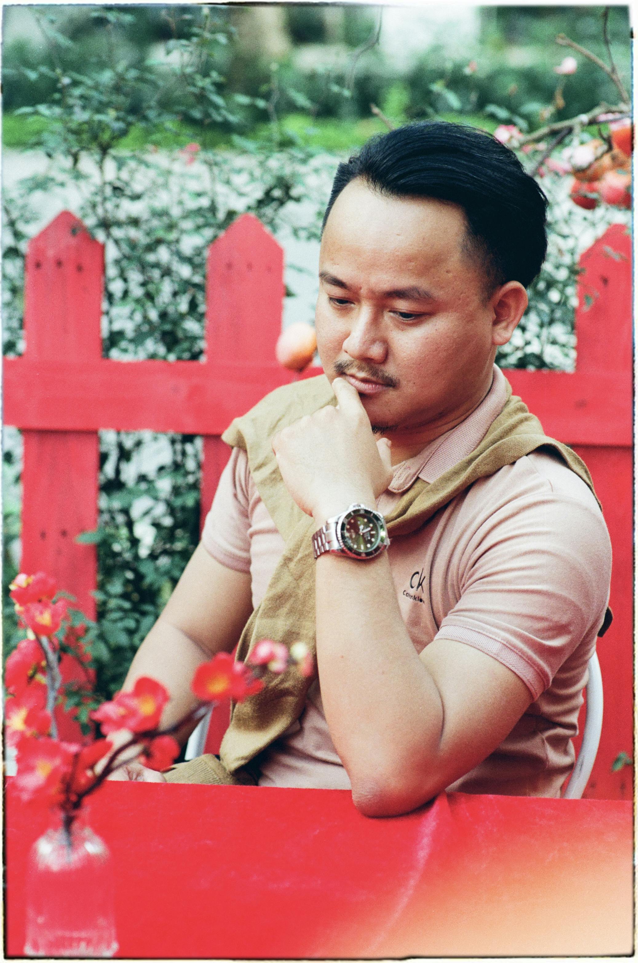 Thoughtful man sitting outdoors at a red table with cherry blossoms, Hanoi, Vietnam.