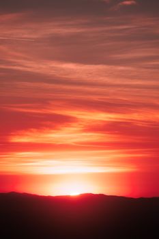 A striking red and orange sunset casting a warm glow over silhouetted hills.
