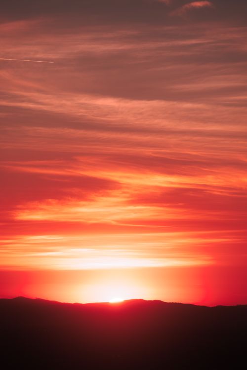Free A striking red and orange sunset casting a warm glow over silhouetted hills. Stock Photo