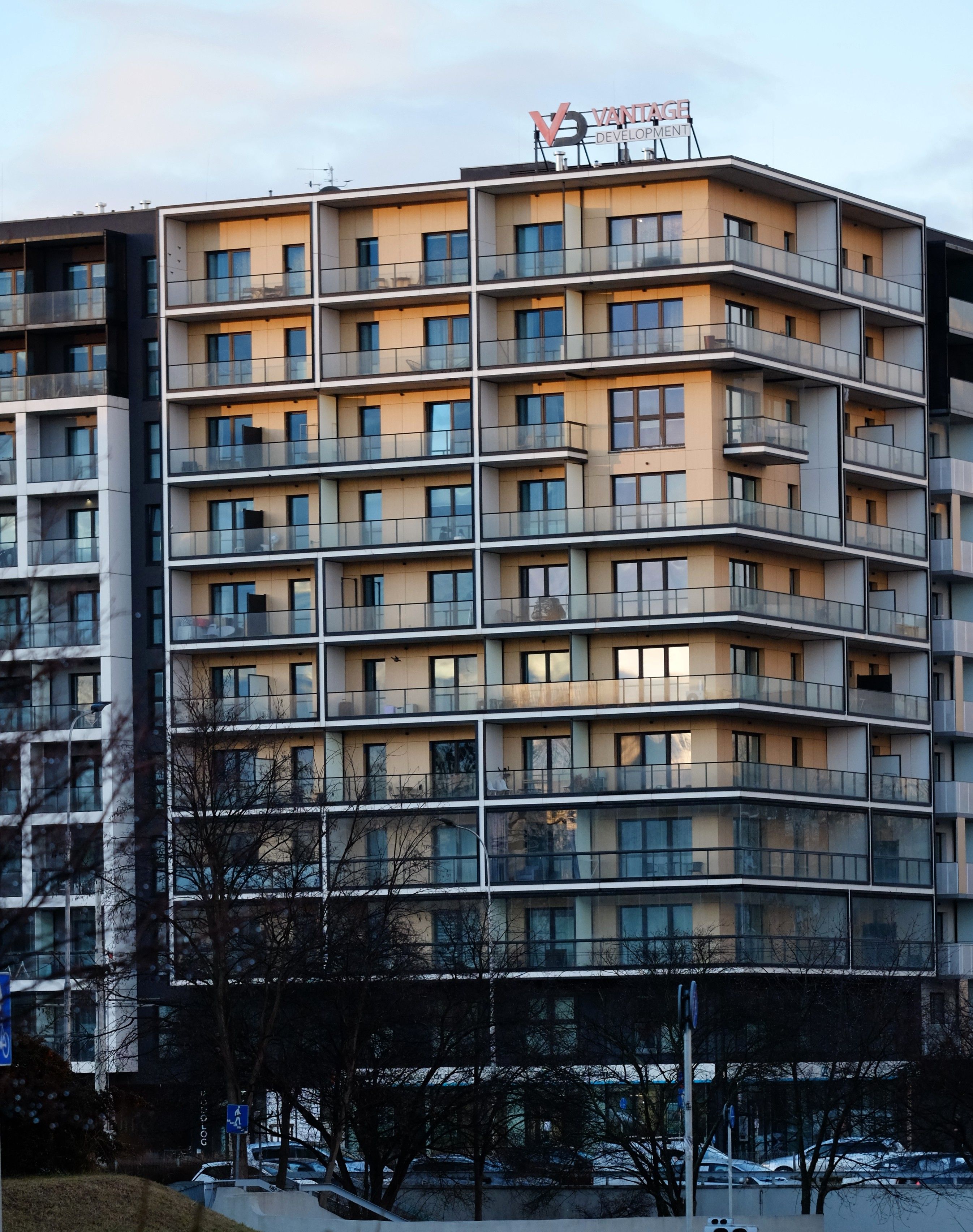 A contemporary multi-story apartment building with balconies and a visible logo captured at sunset.